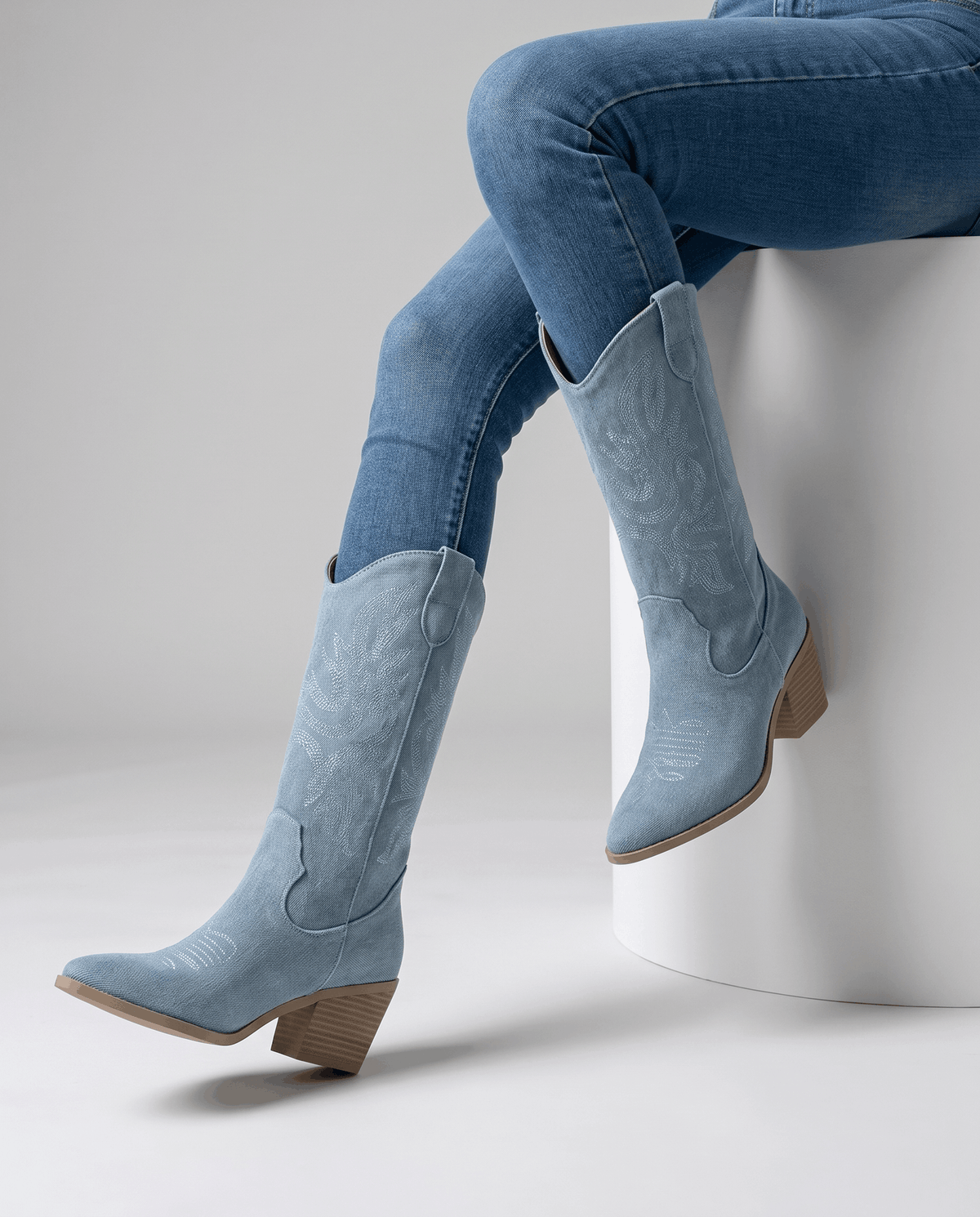 Seated legs in blue jeans and light blue boots with pointed toes against a grey backdrop