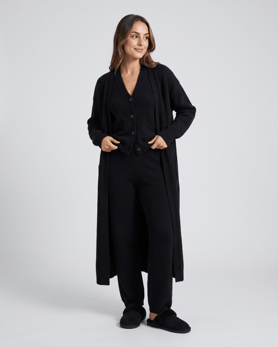 Black long cardigan coat, knit vest and wide-leg pants with hands in the pockets