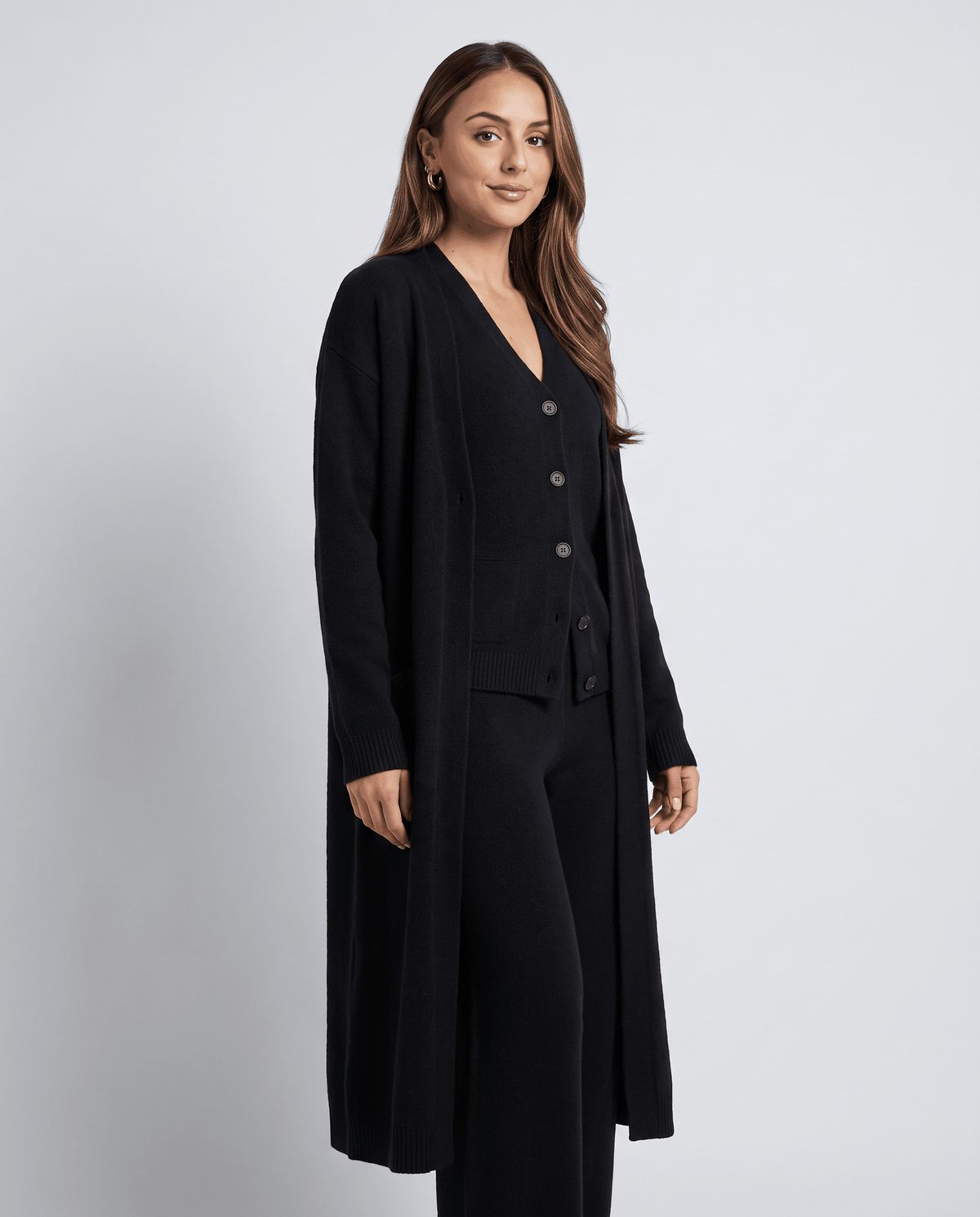 Three-quarter view of the black cardigan coat, buttoned vest and wide-leg pants