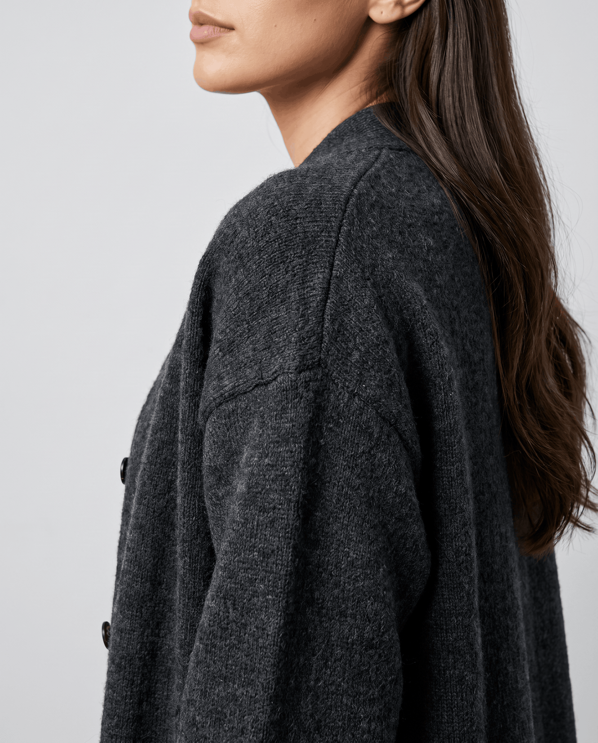 Close-up of the dropped shoulder and button detail on the dark gray cardigan coat