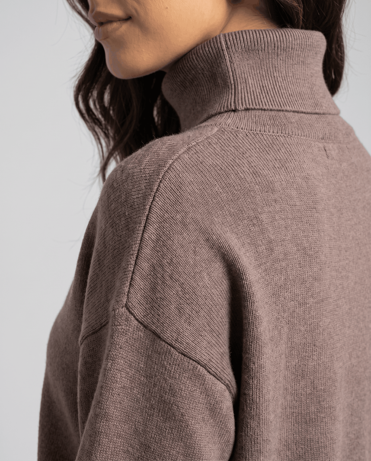 Side close-up of the turtleneck collar and drop-shoulder seam on the taupe knit top