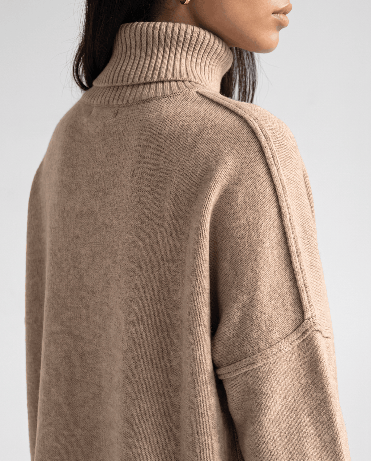 Close-up of the beige knit turtleneck collar and drop shoulder seam from behind