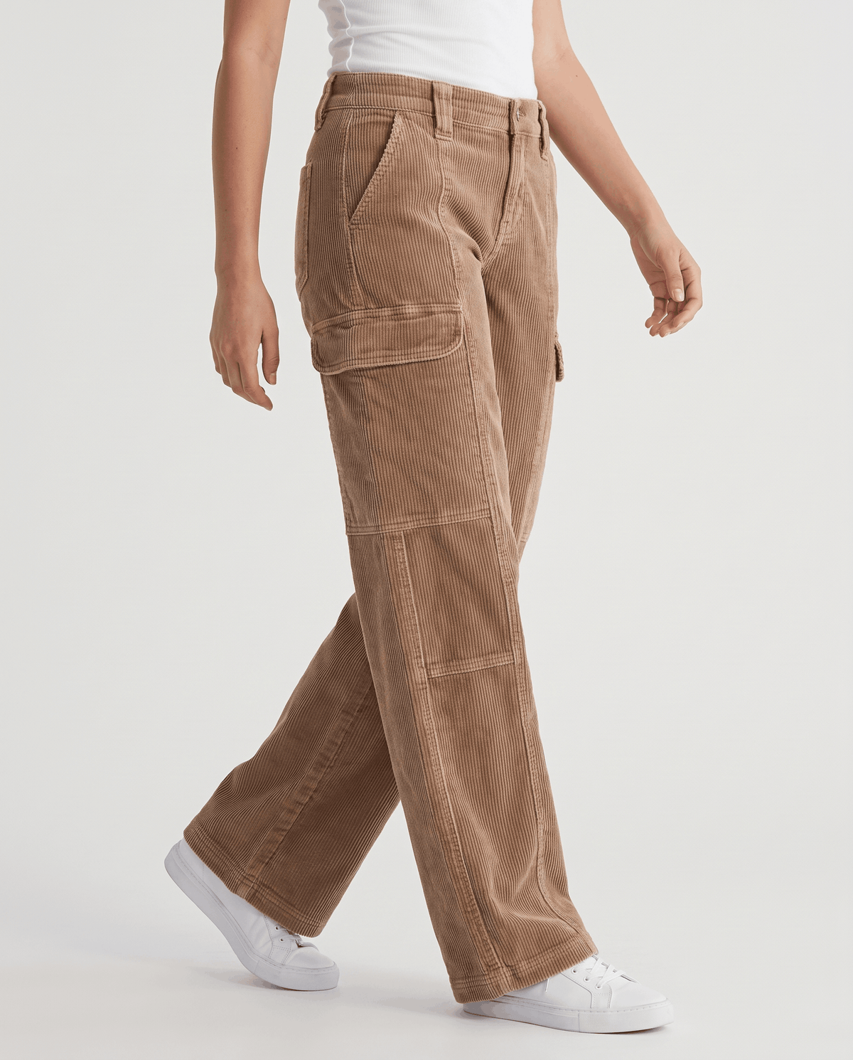 Woman wearing tan wide-leg corduroy cargo pants mid-stride with white sneakers, side view