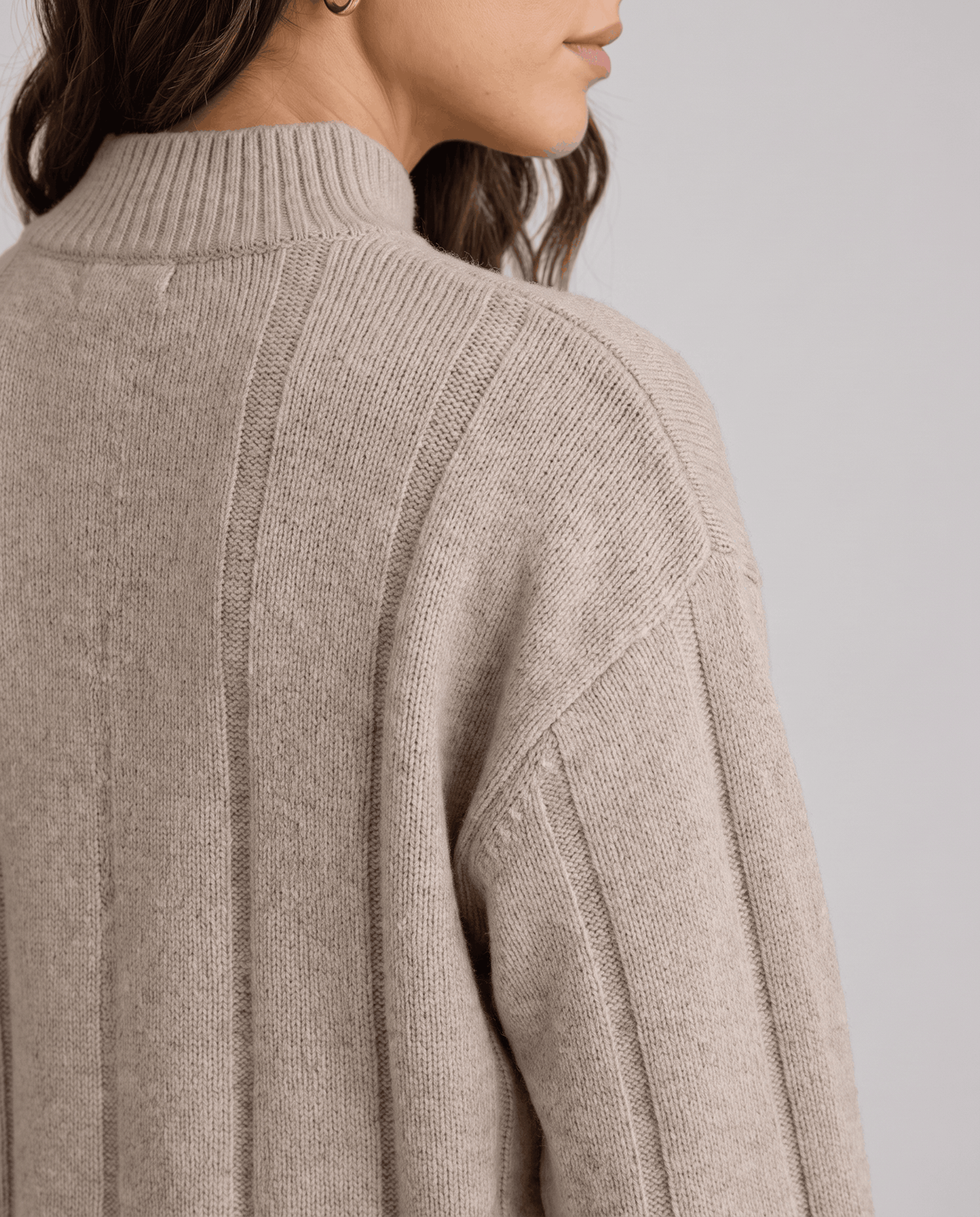 Close-up of wide vertical ribbing and drop-shoulder seam on the beige knit top