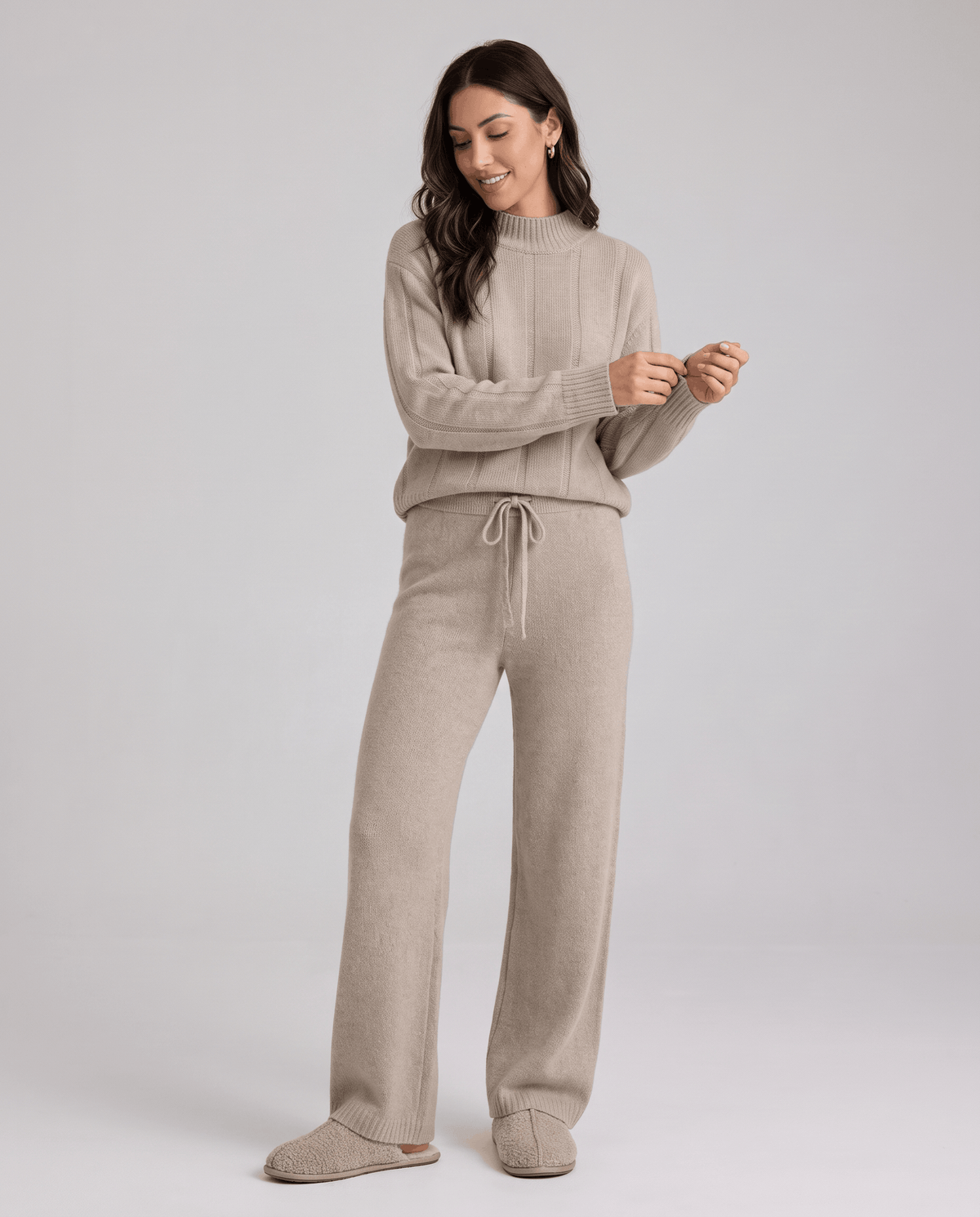 Beige knit set with the model adjusting her sleeve cuff, full-length front view