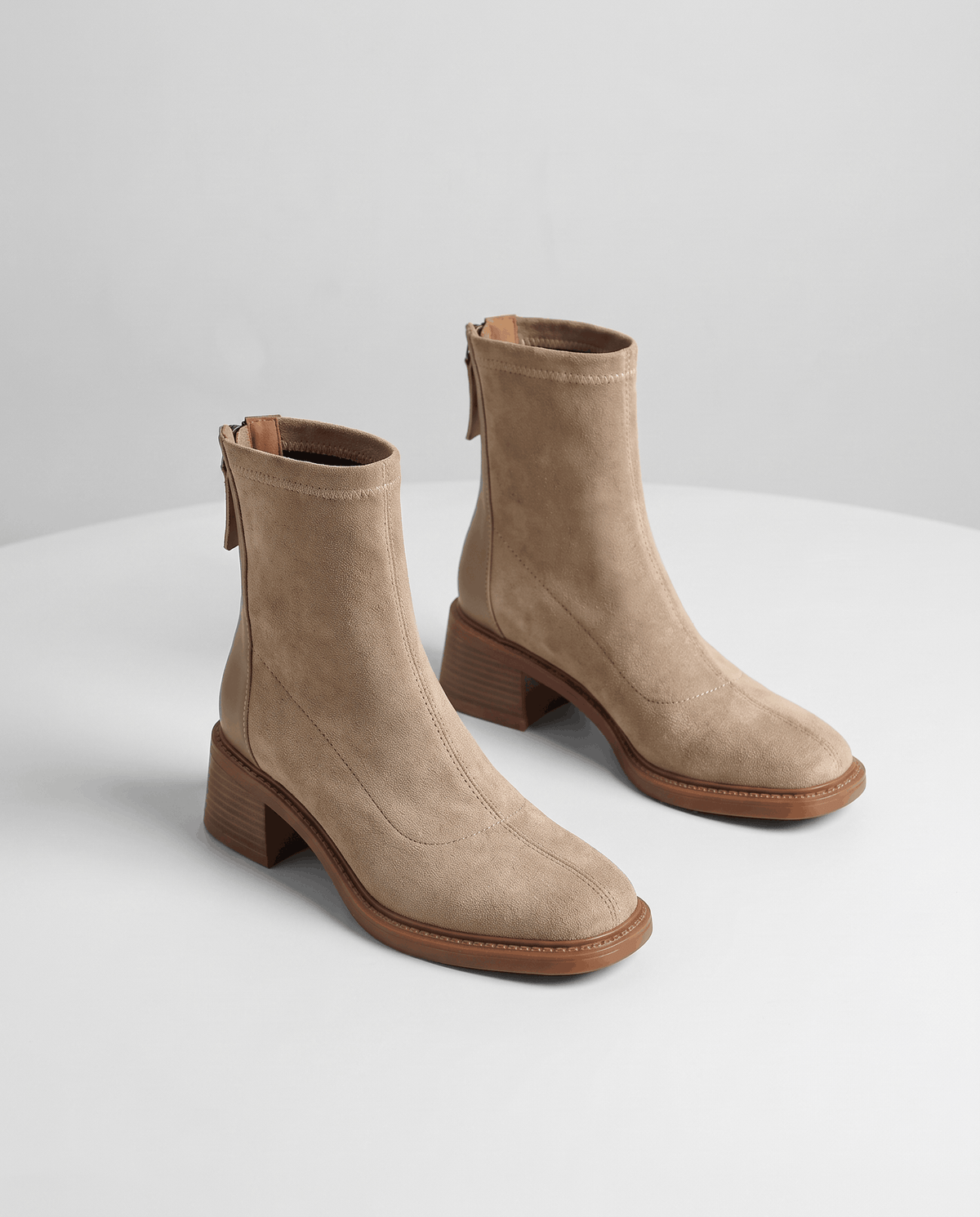 Beige suede ankle boots angled to show the back zip and block heel