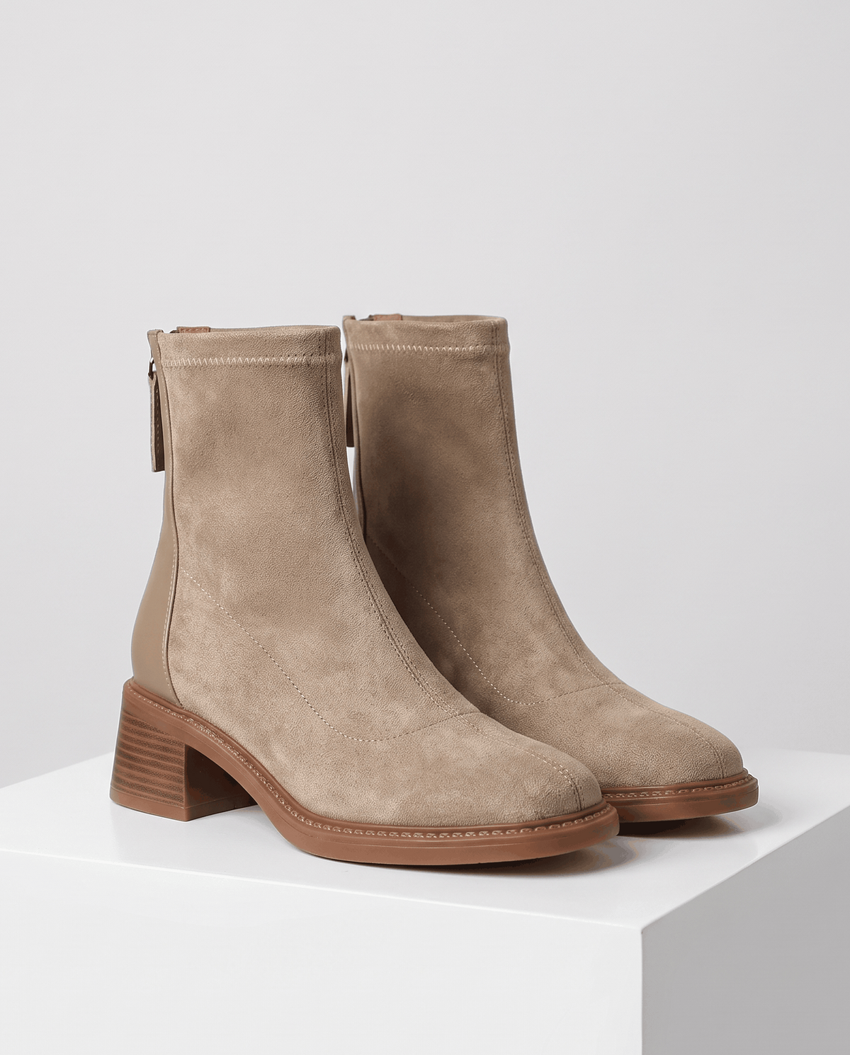 Pair of beige suede block heel ankle boots with stretch shaft on a white block