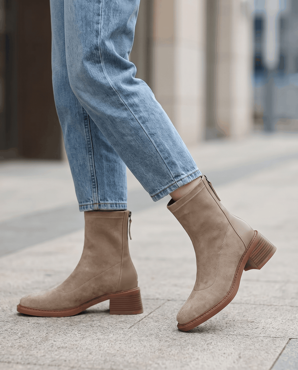 Woman wearing beige suede block heel ankle boots with blue jeans on a city pavement