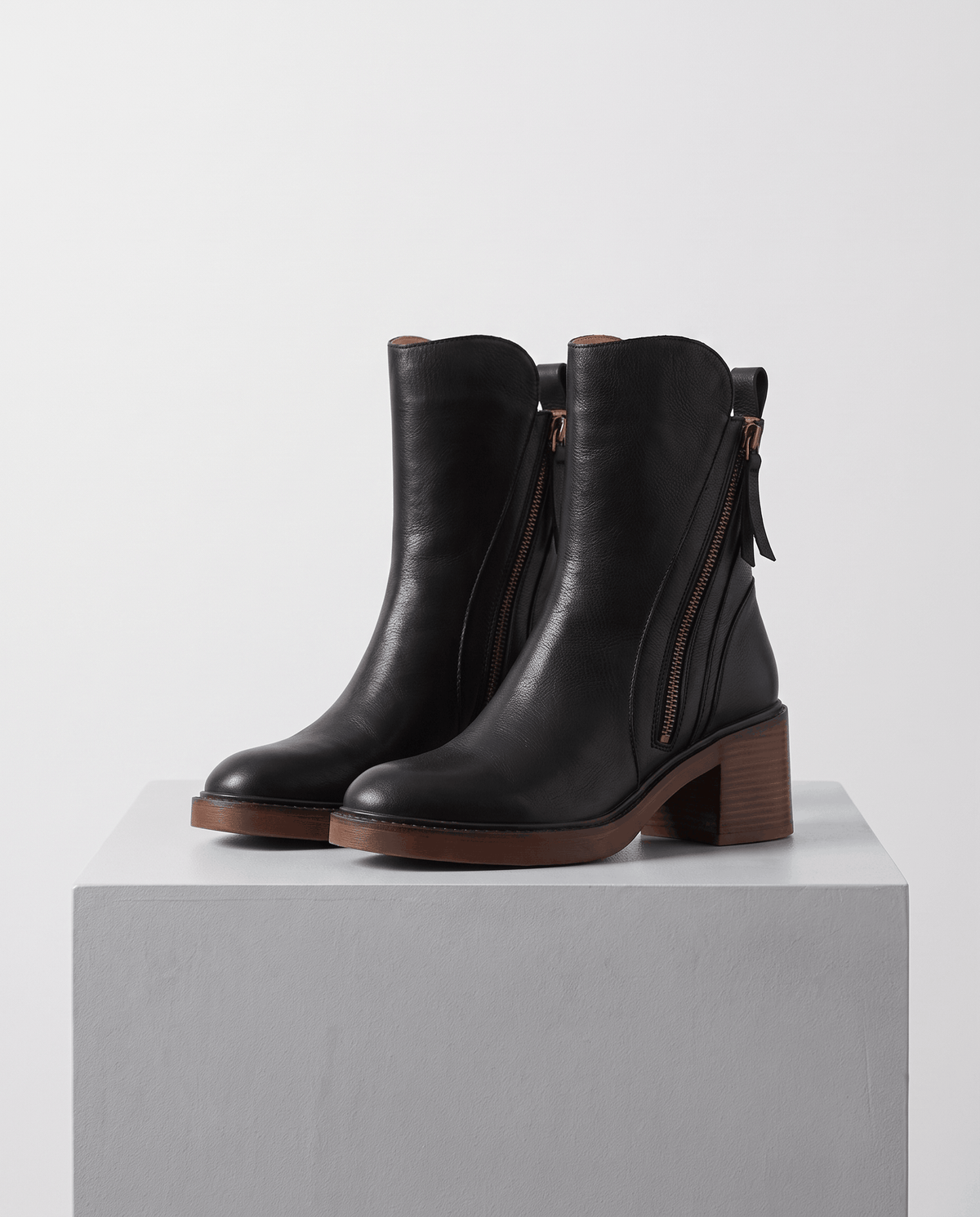 Pair of black block heel ankle boots with side zip on a gray block