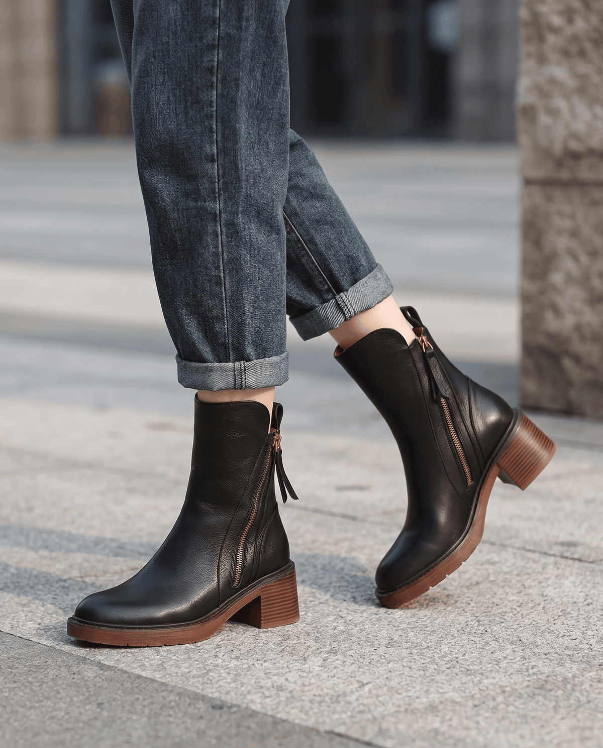Woman wearing black block heel ankle boots with rolled blue jeans on a city street