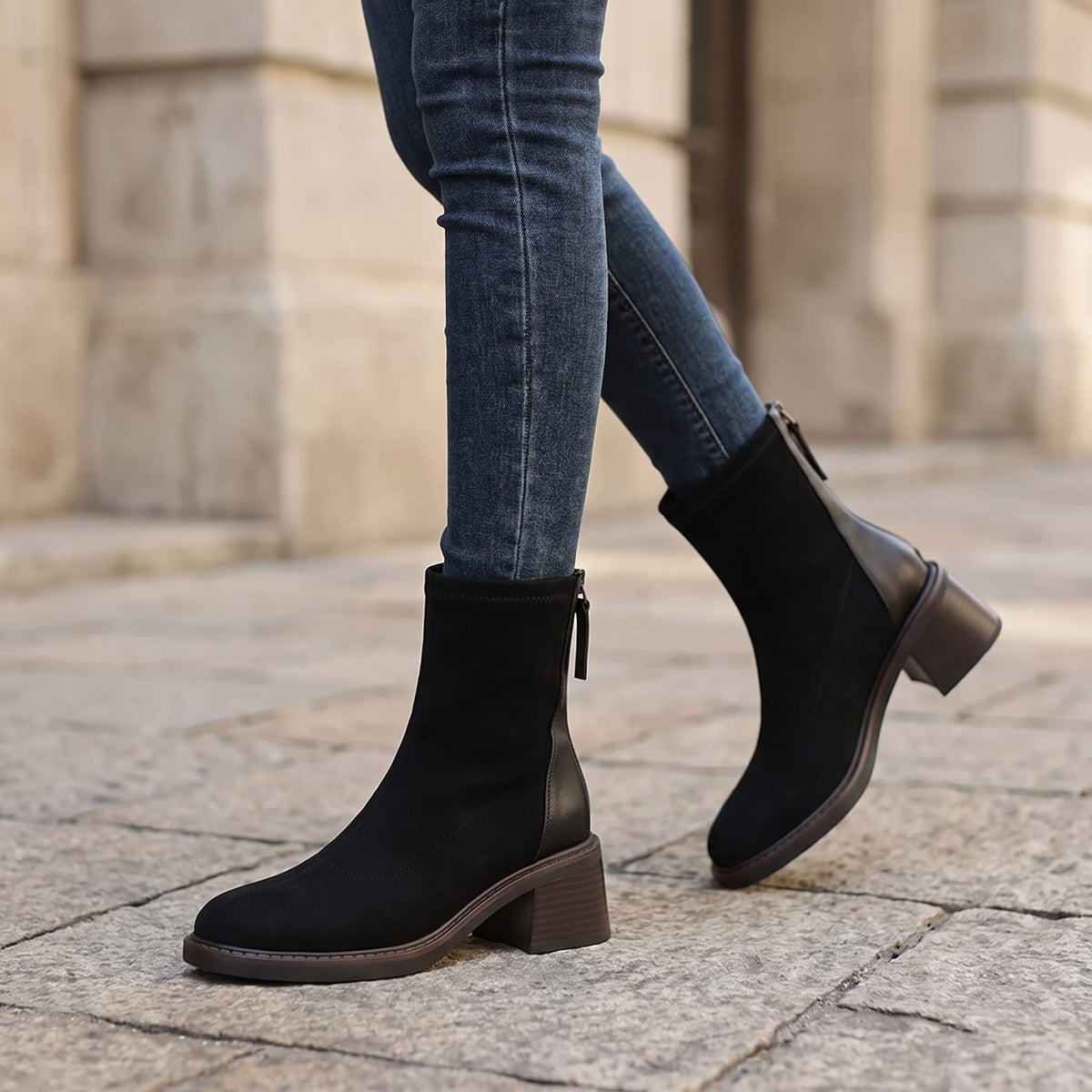 Woman wearing black suede block heel ankle boots with blue jeans on a city street