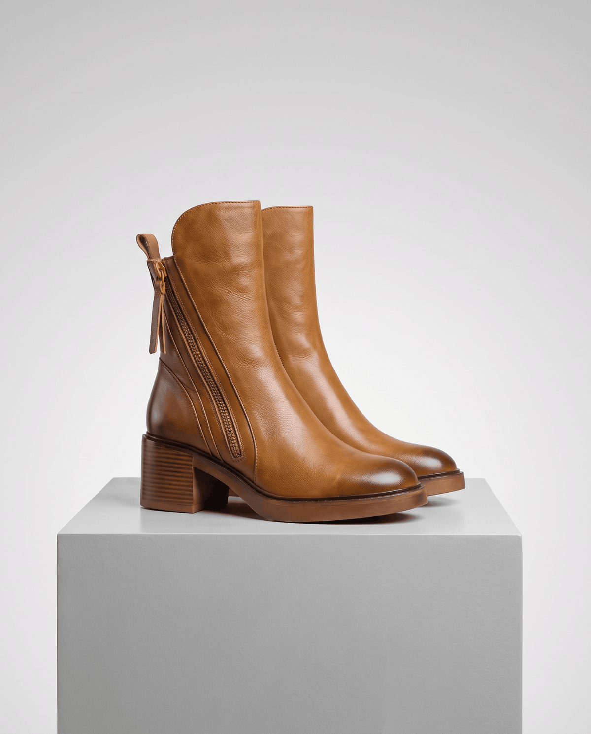 Brown block heel ankle boots angled on a gray block to show the tapered toe