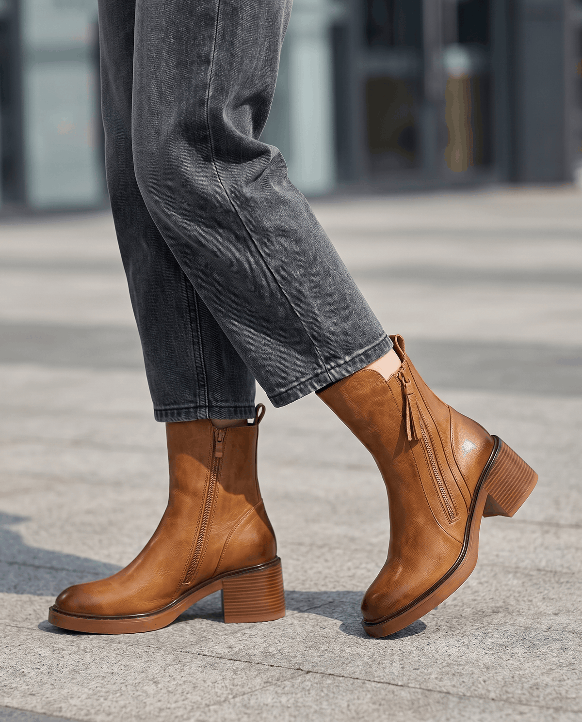 Woman wearing brown block heel ankle boots with rolled blue jeans on a city pavement