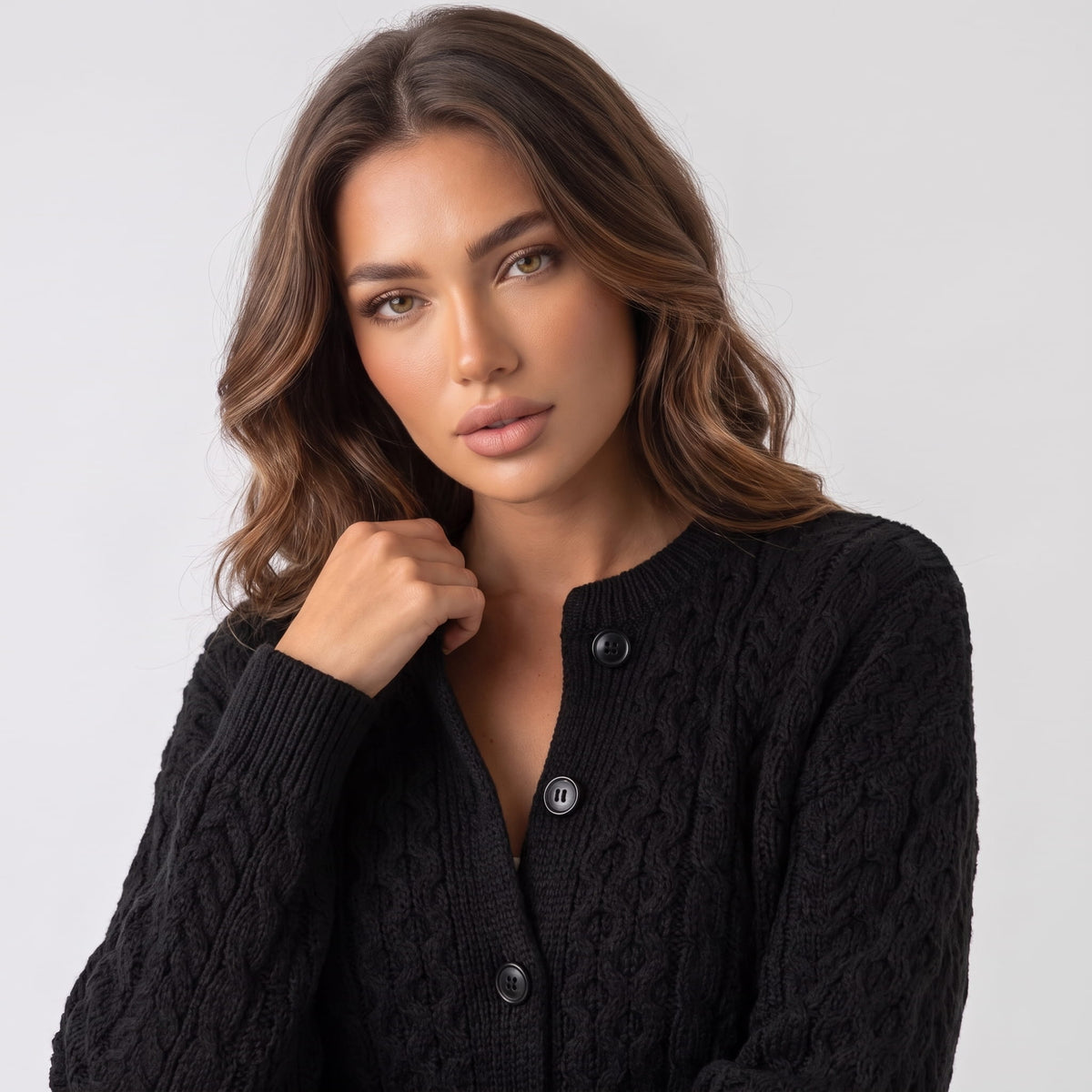 Black cable-knit cardigan with hand at the collar showing buttons and cable pattern