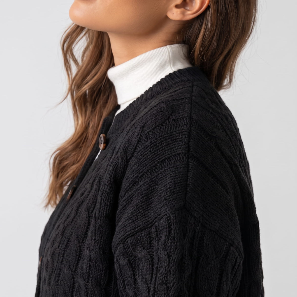 Close side view of black cable-knit cardigan sleeve and shoulder