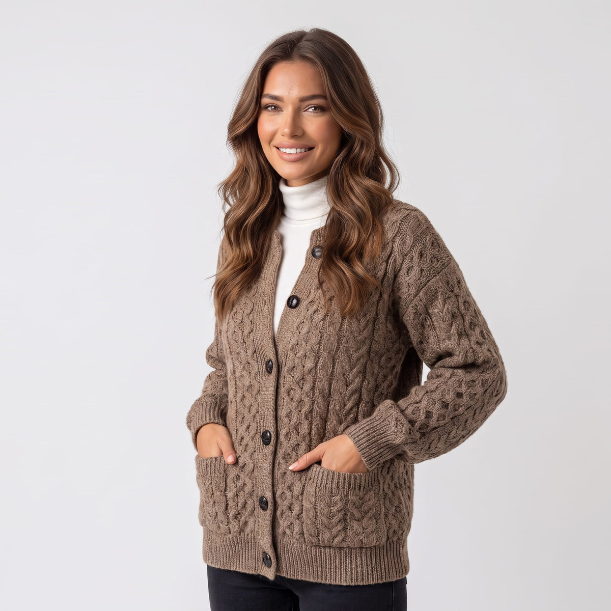 Women's camel cable-knit button cardigan with front pockets worn over a white turtleneck