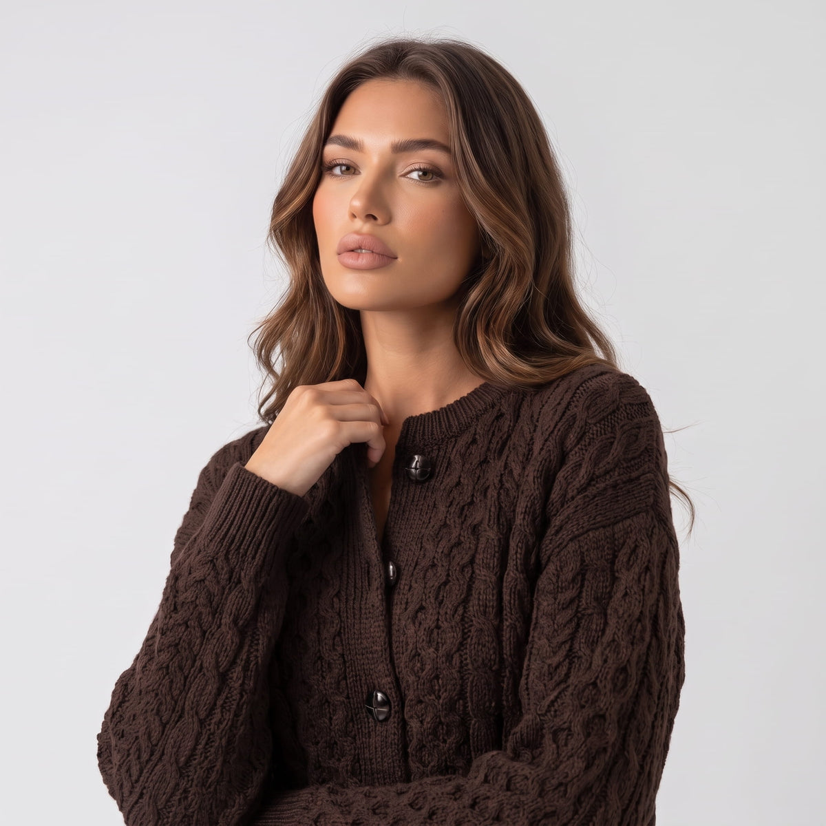Dark brown cable-knit cardigan with hand at the collar showing buttons and cable pattern
