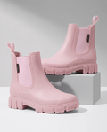 Pink Chelsea-style ankle boots with elastic side panels and chunky lug soles displayed on white blocks.