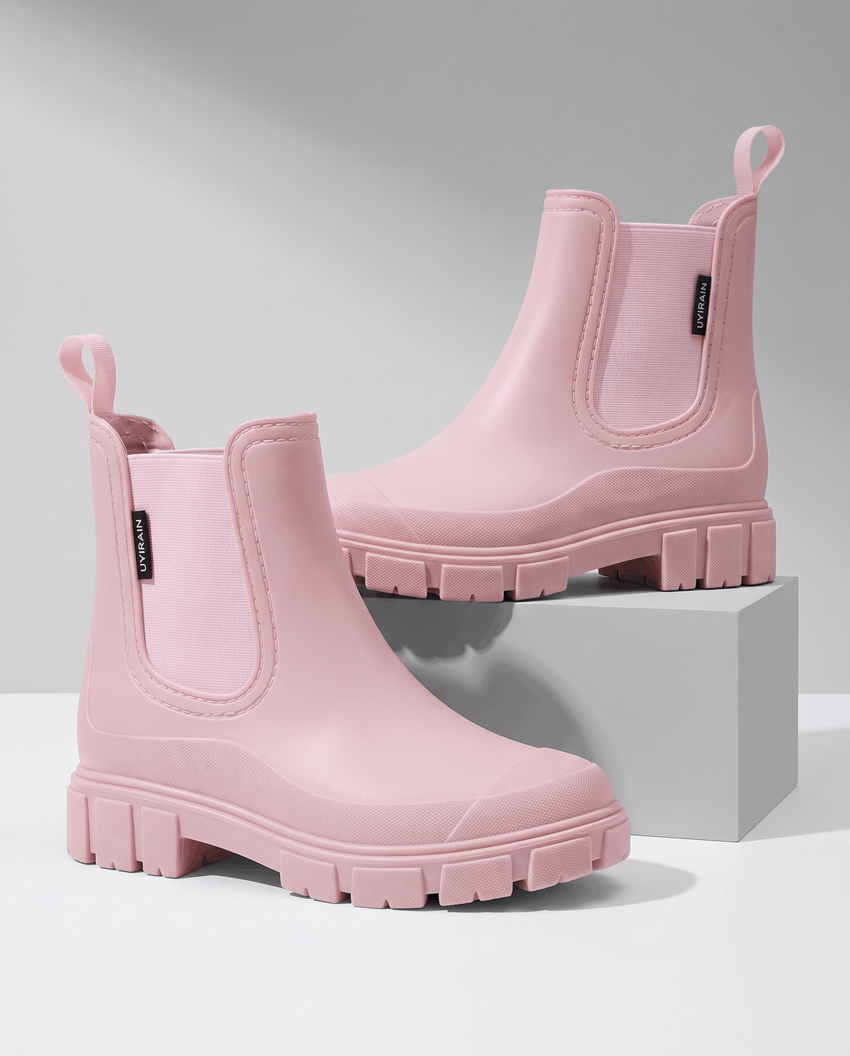 Pink Chelsea-style ankle boots with elastic side panels and chunky lug soles displayed on white blocks.