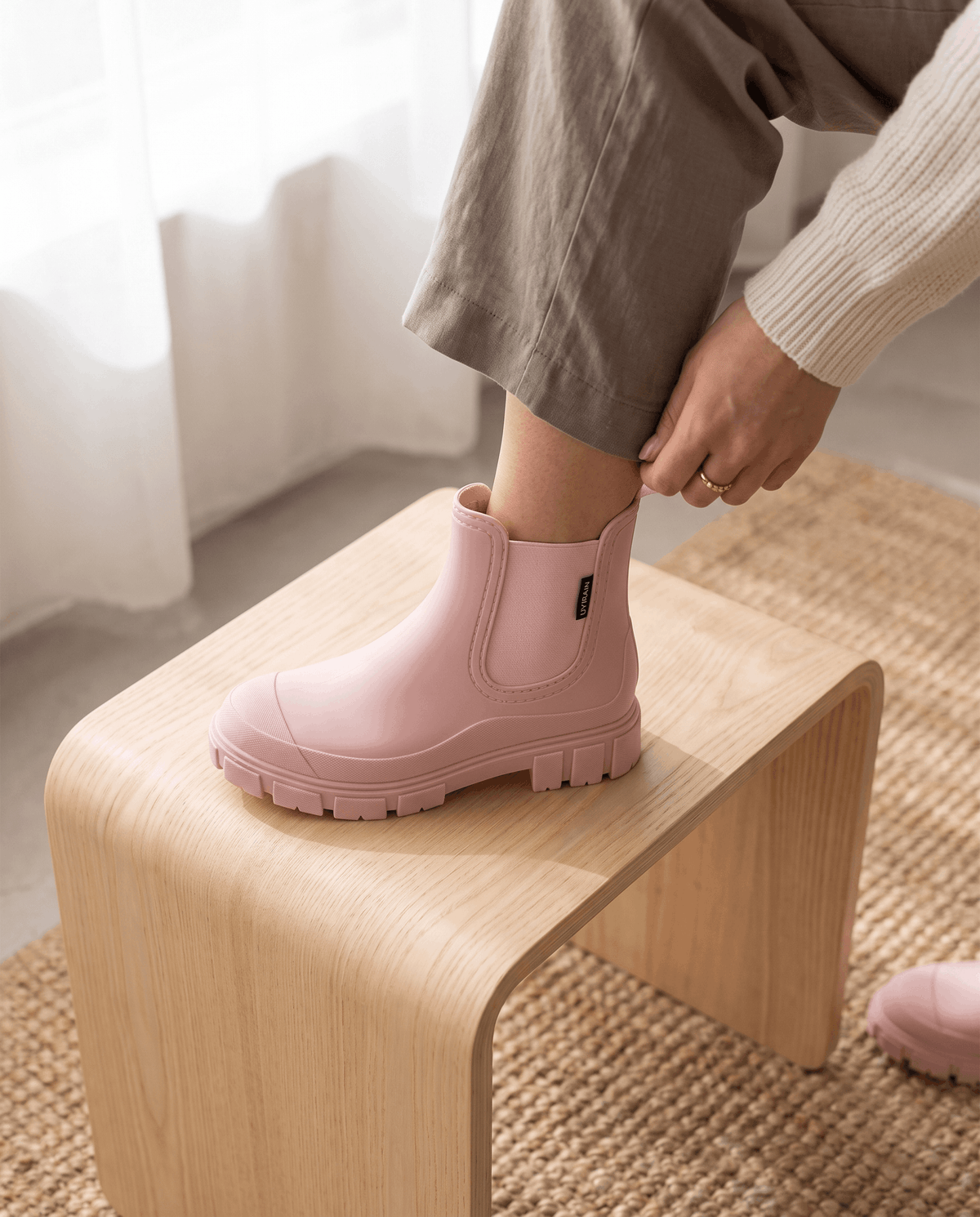 Person wearing pink Chelsea ankle boots with beige trousers indoors.