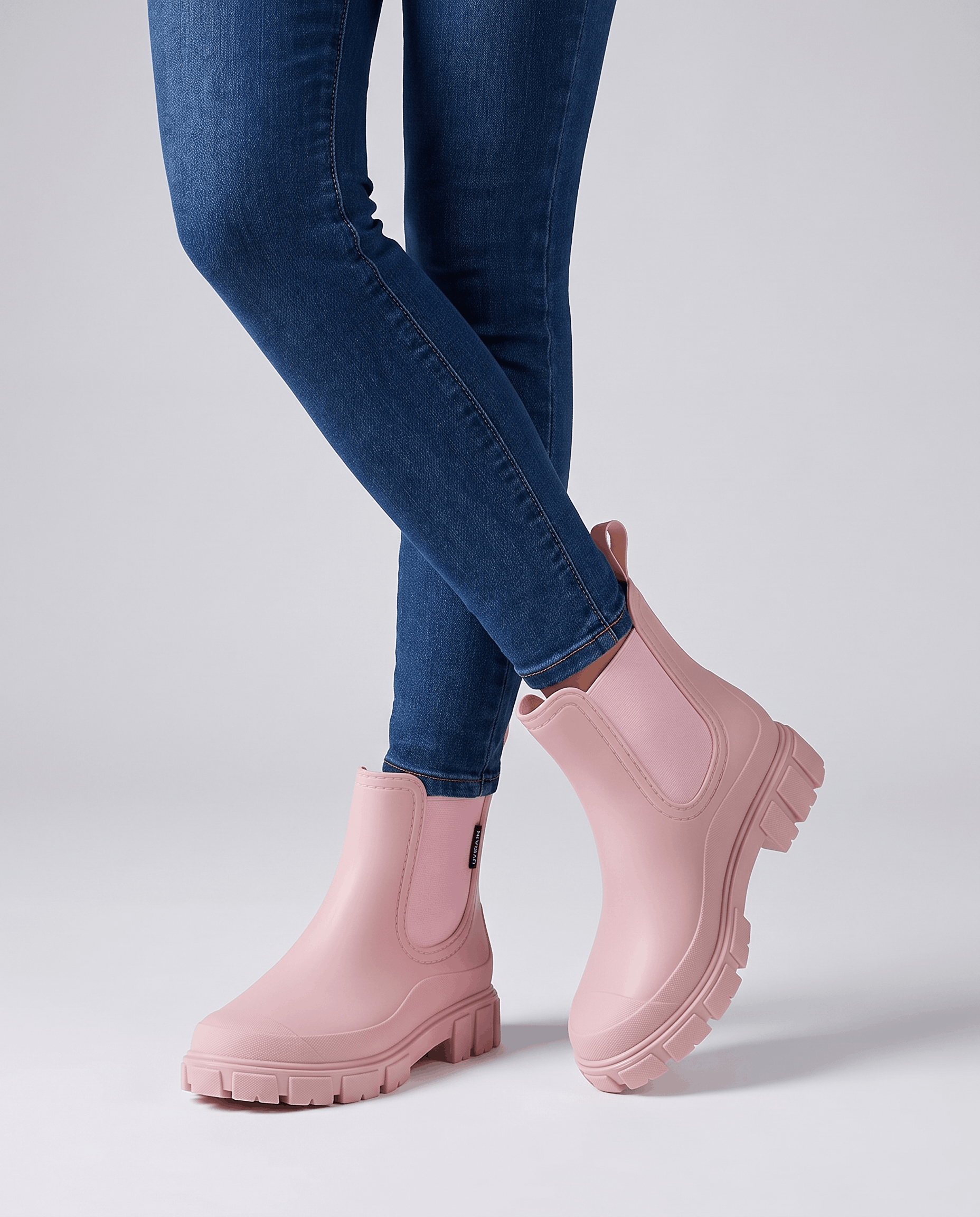 Person wearing pink Chelsea ankle boots with blue jeans in a studio setting.