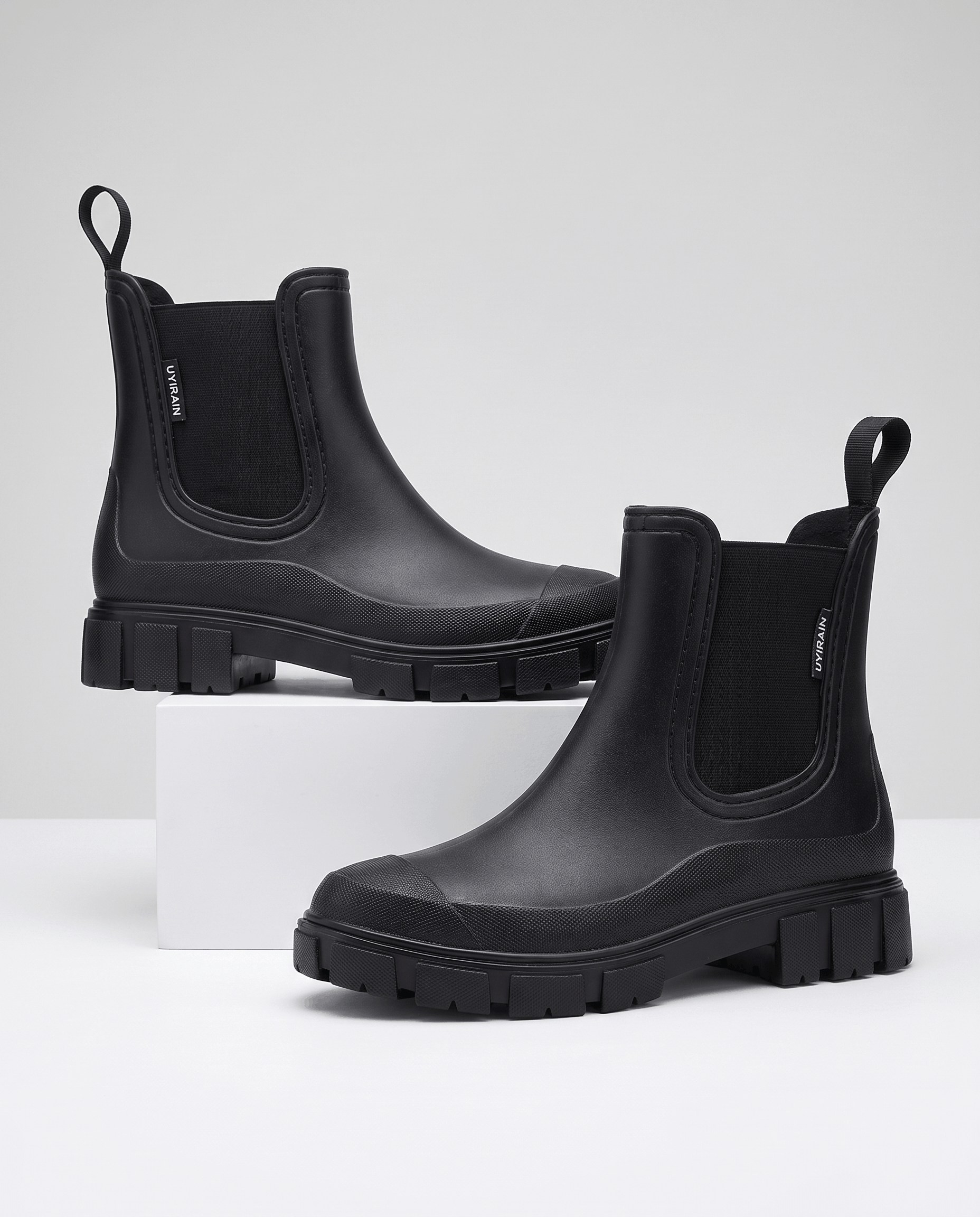 Black Chelsea-style ankle boots with chunky lug soles displayed on white blocks.