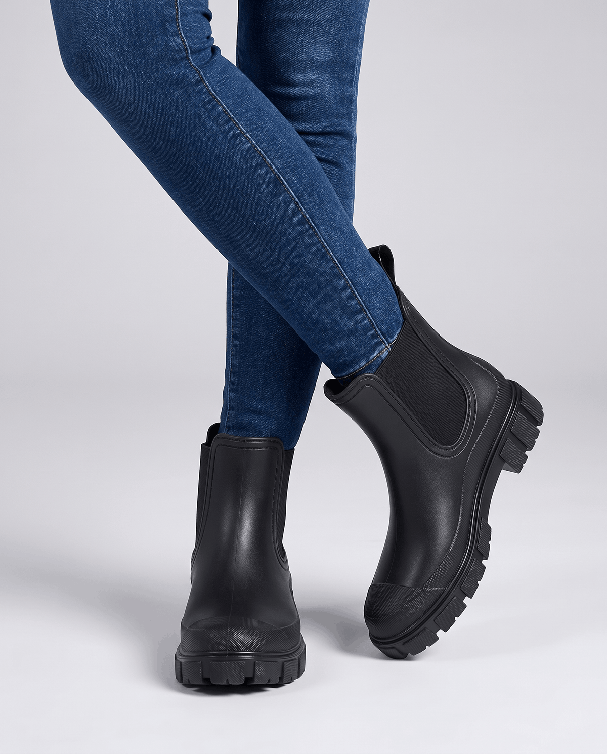 Person wearing black Chelsea ankle boots with beige trousers indoors.
