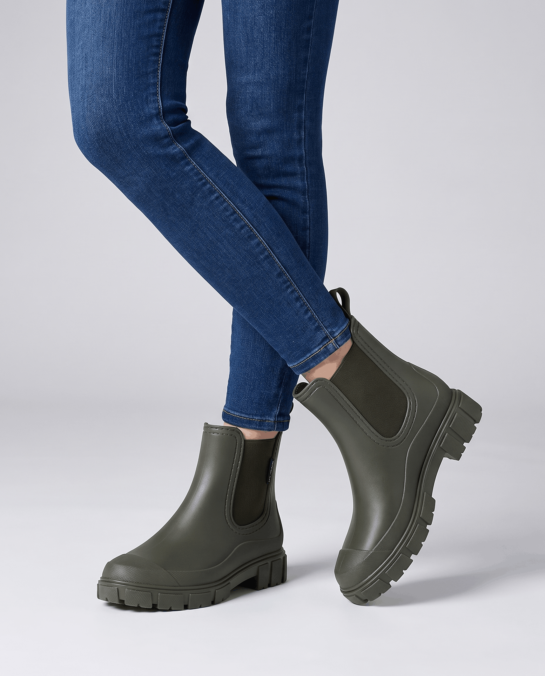 Green Chelsea boots with chunky lug soles worn with blue jeans.