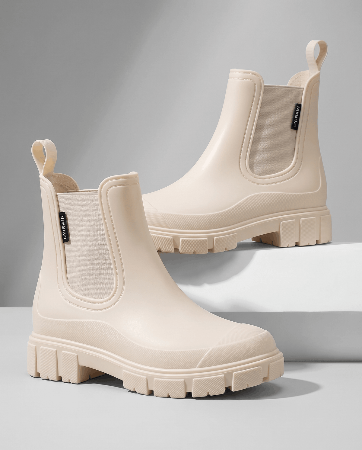 Beige Chelsea boots with chunky lug soles displayed on white blocks.