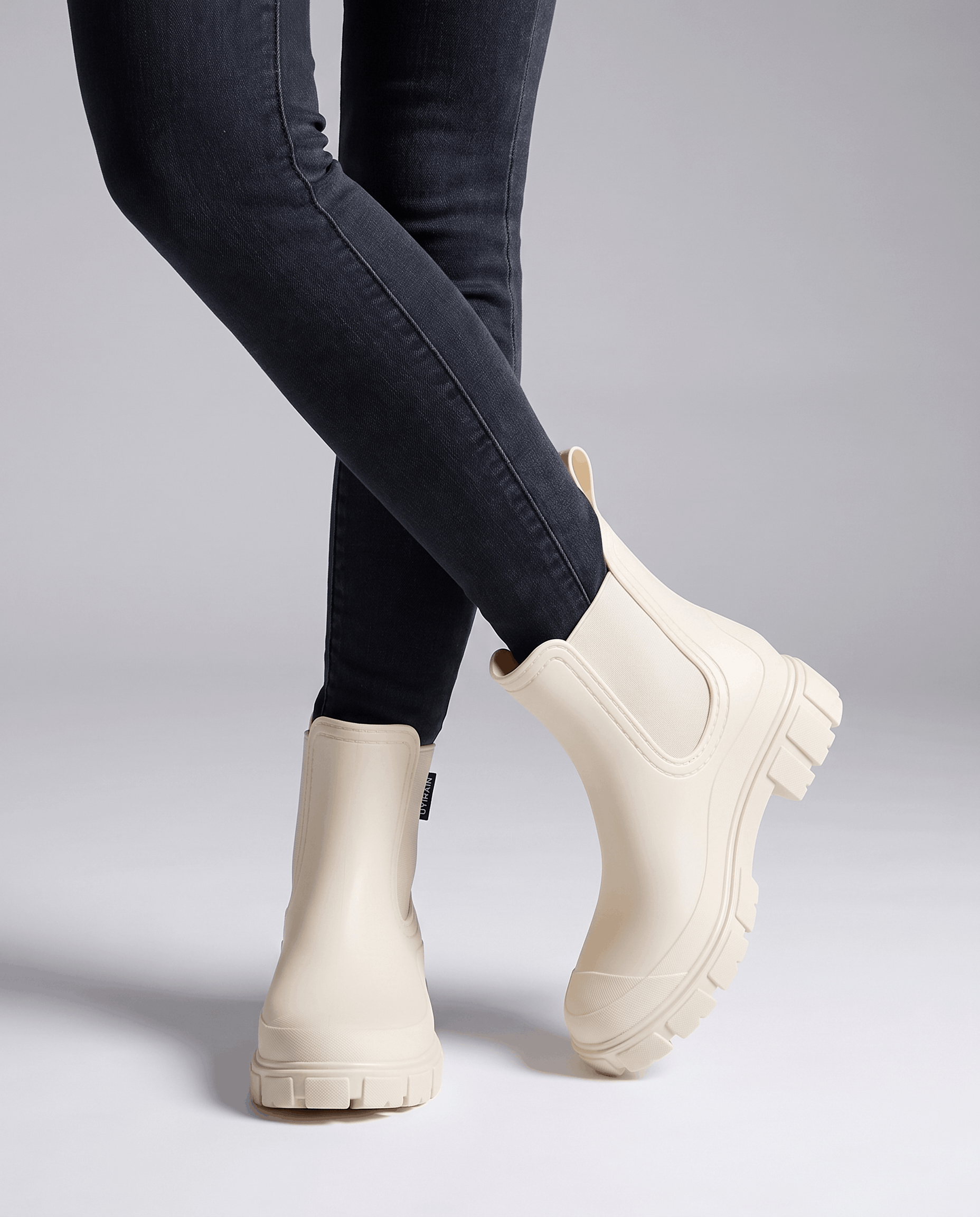Person wearing beige Chelsea boots with dark leggings in a studio setting.