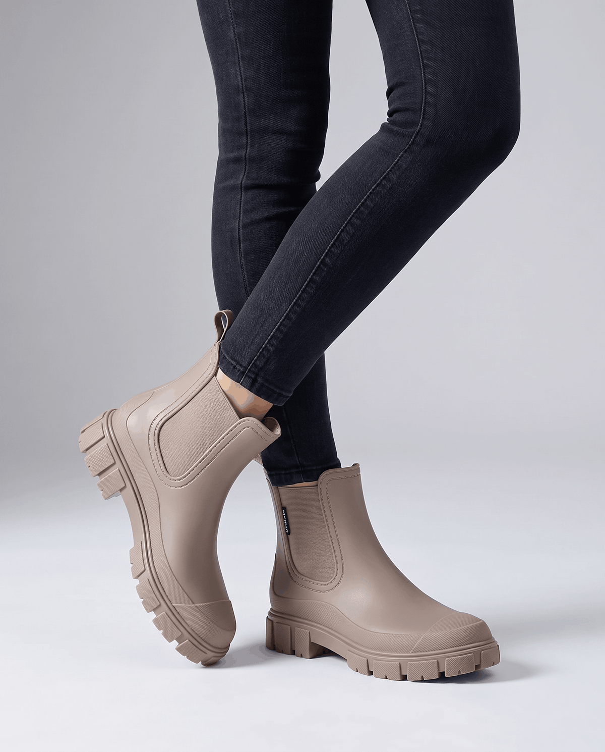 Person wearing white taupe boots with dark jeans in a studio setting.
