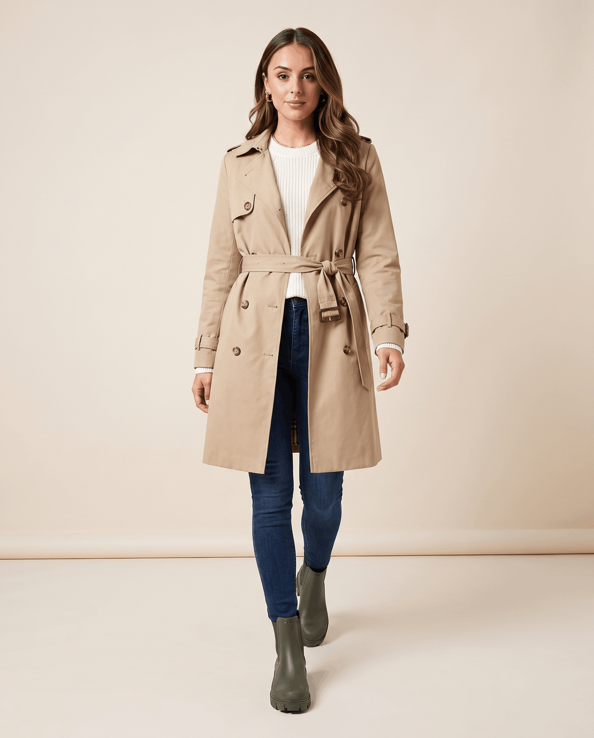 Woman wearing olive green Chelsea boots with a beige trench coat.