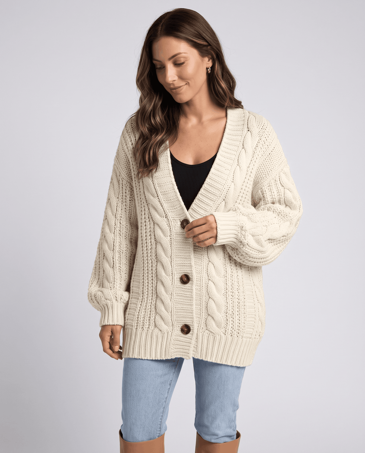 Three-quarter view of a cream cable knit cardigan with a deep V neck