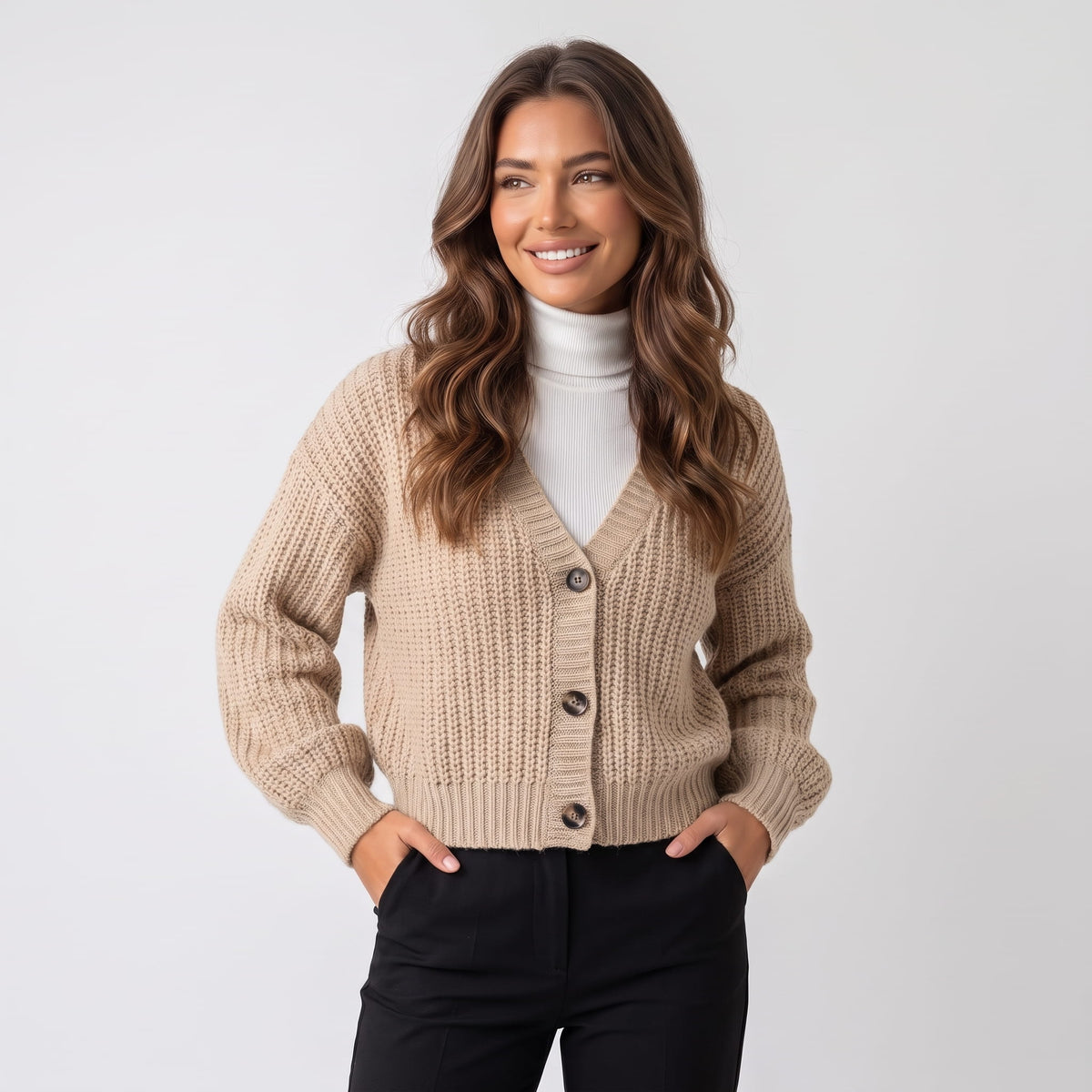 Women's beige chunky knit button cardigan worn over a white turtleneck and black trousers