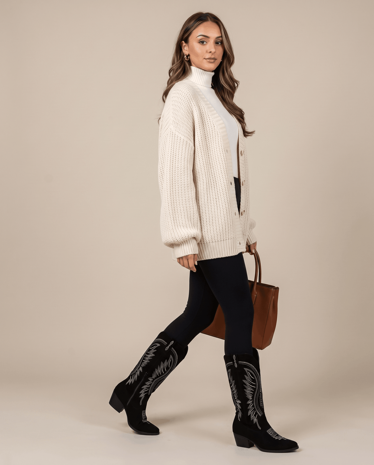 Woman in a cream cardigan and black leggings wearing black cowboy boots