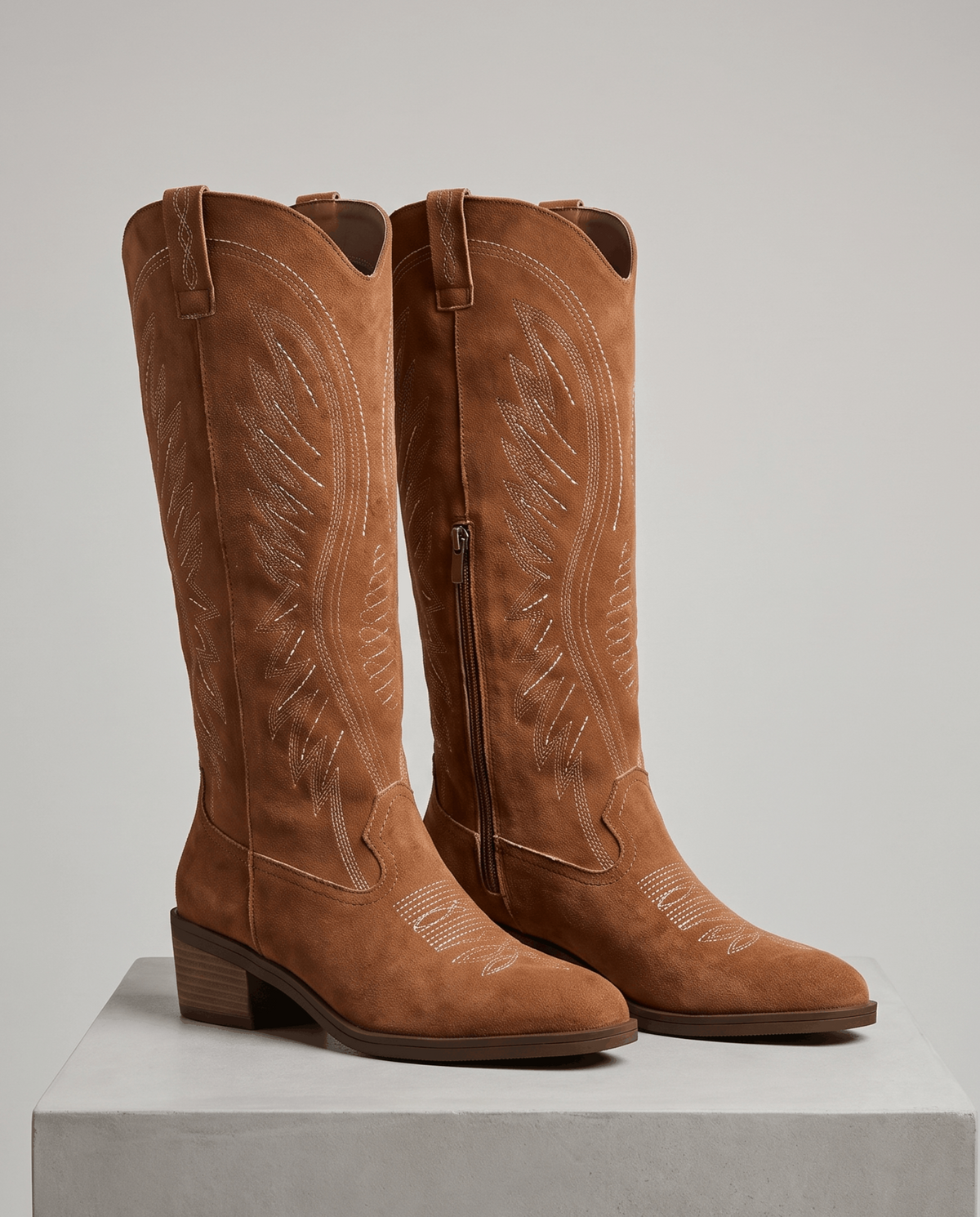 Embroidered knee-high cowboy boots in brown suede on a white display block