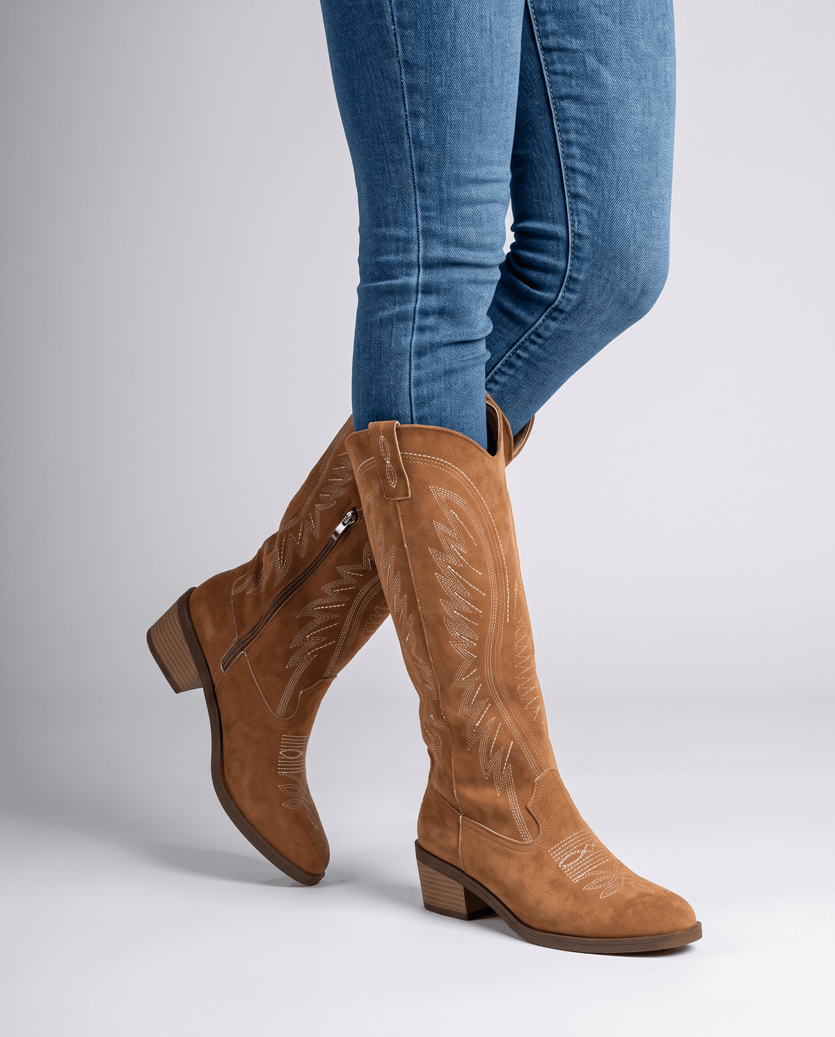 Woman in blue jeans tucked into brown embroidered boots, side view