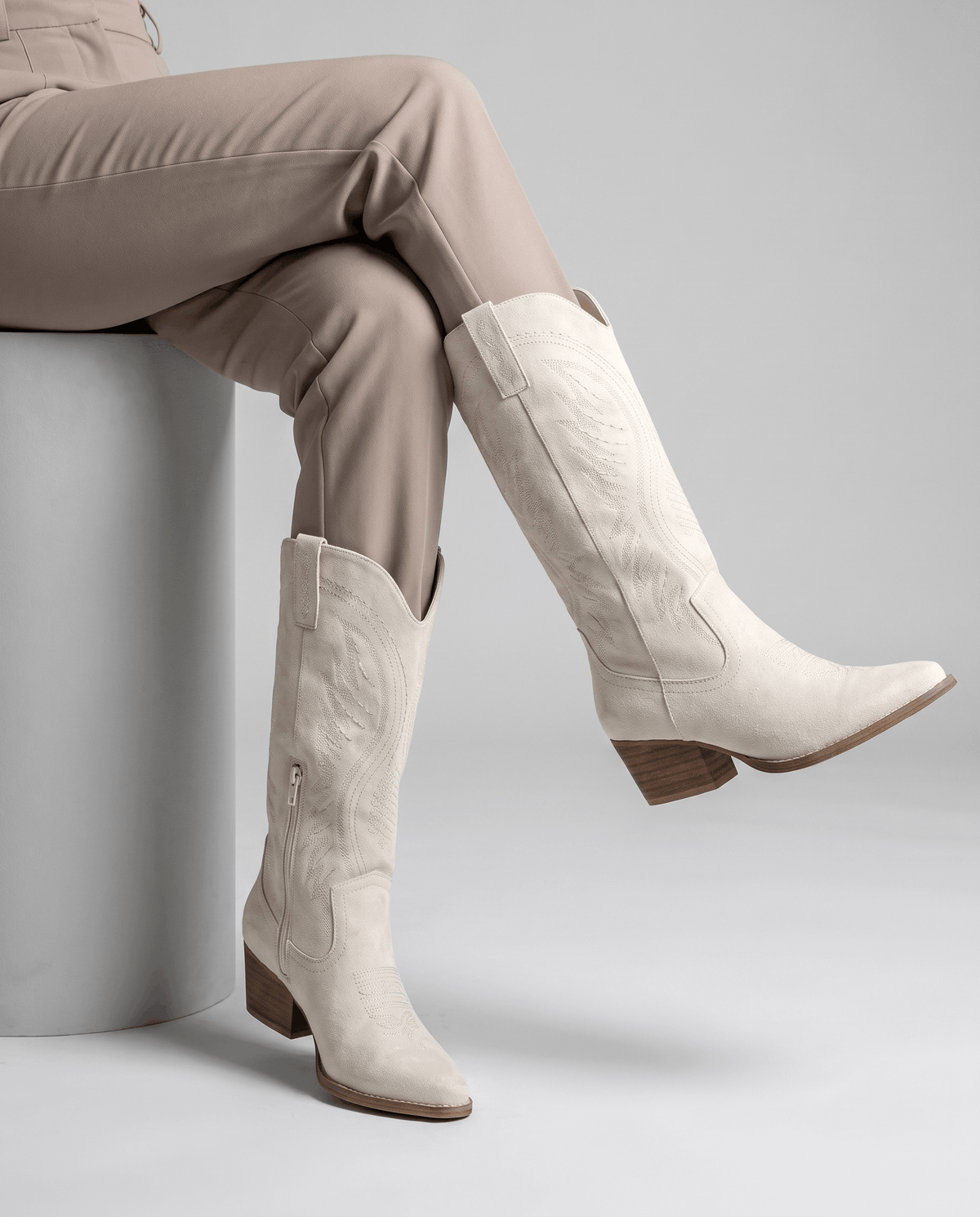Seated woman in taupe trousers wearing cream western boots