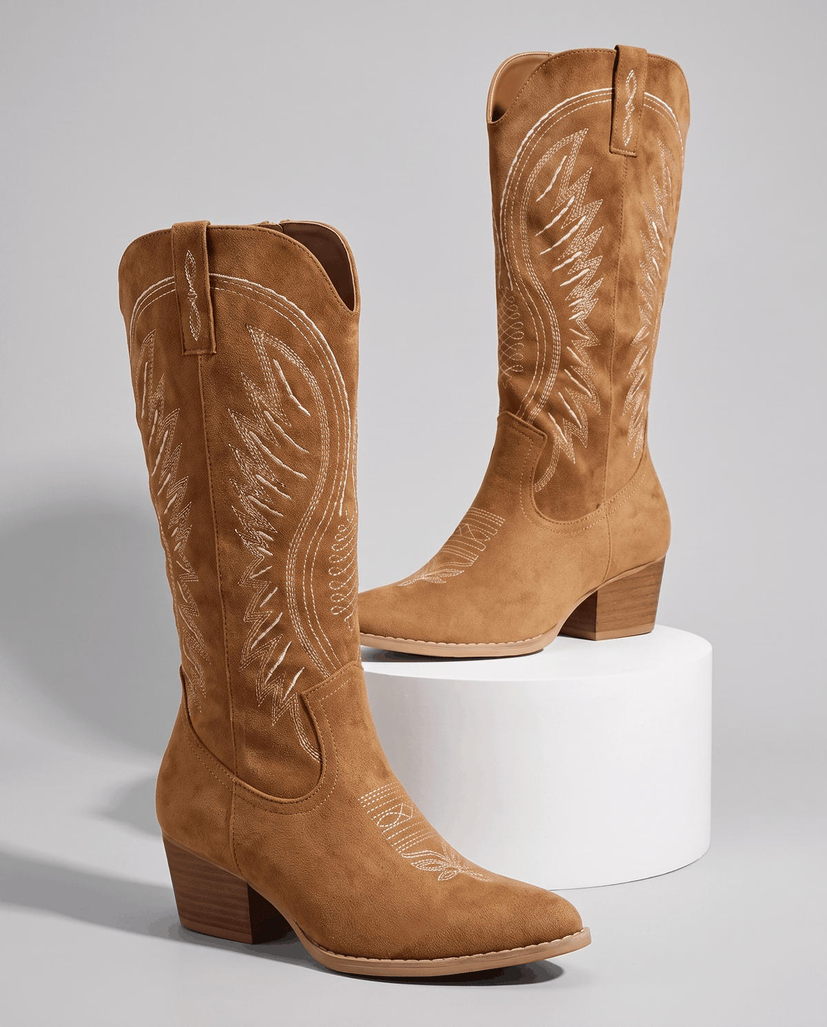 Brown suede-look cowboy boots displayed on a white pedestal