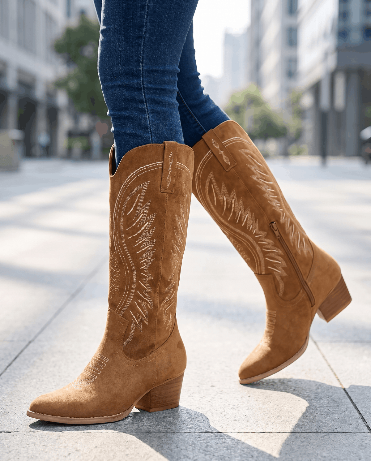 Brown western boots worn walking on a sunny city sidewalk with dark tucked jeans
