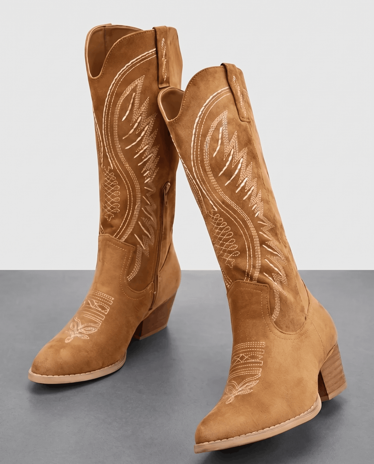 Pair of brown embroidered western boots with stacked heels on a grey studio floor