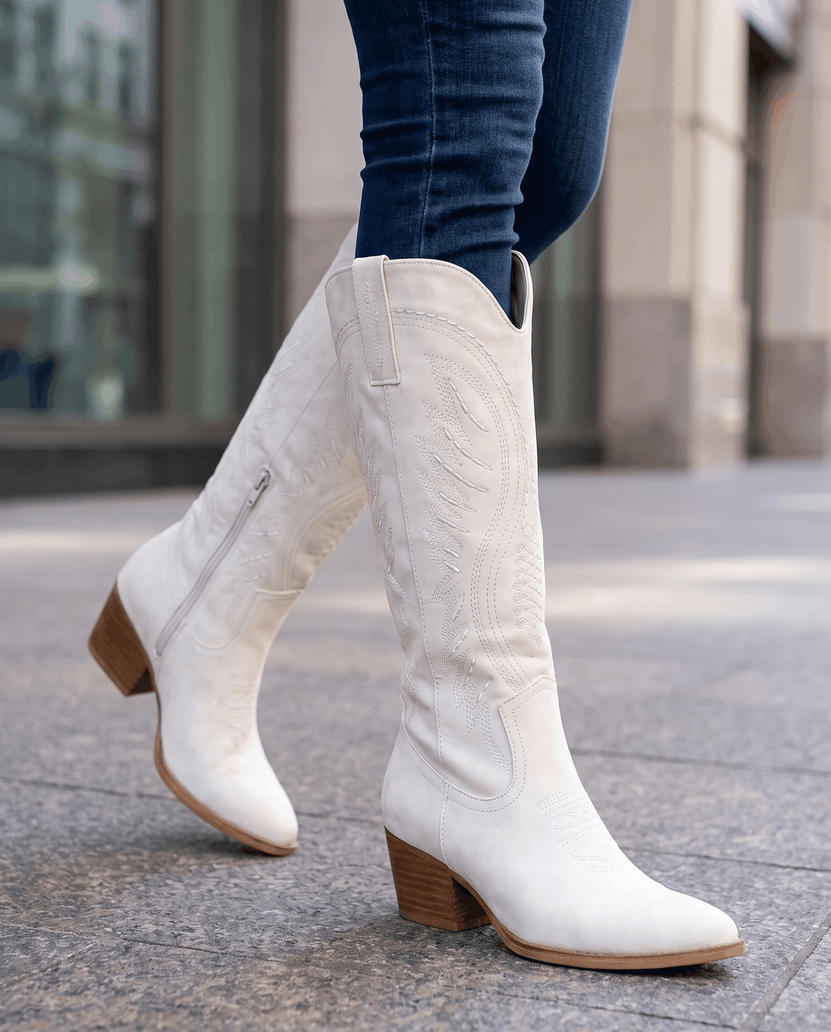White western boots worn walking on a city sidewalk with tucked blue jeans