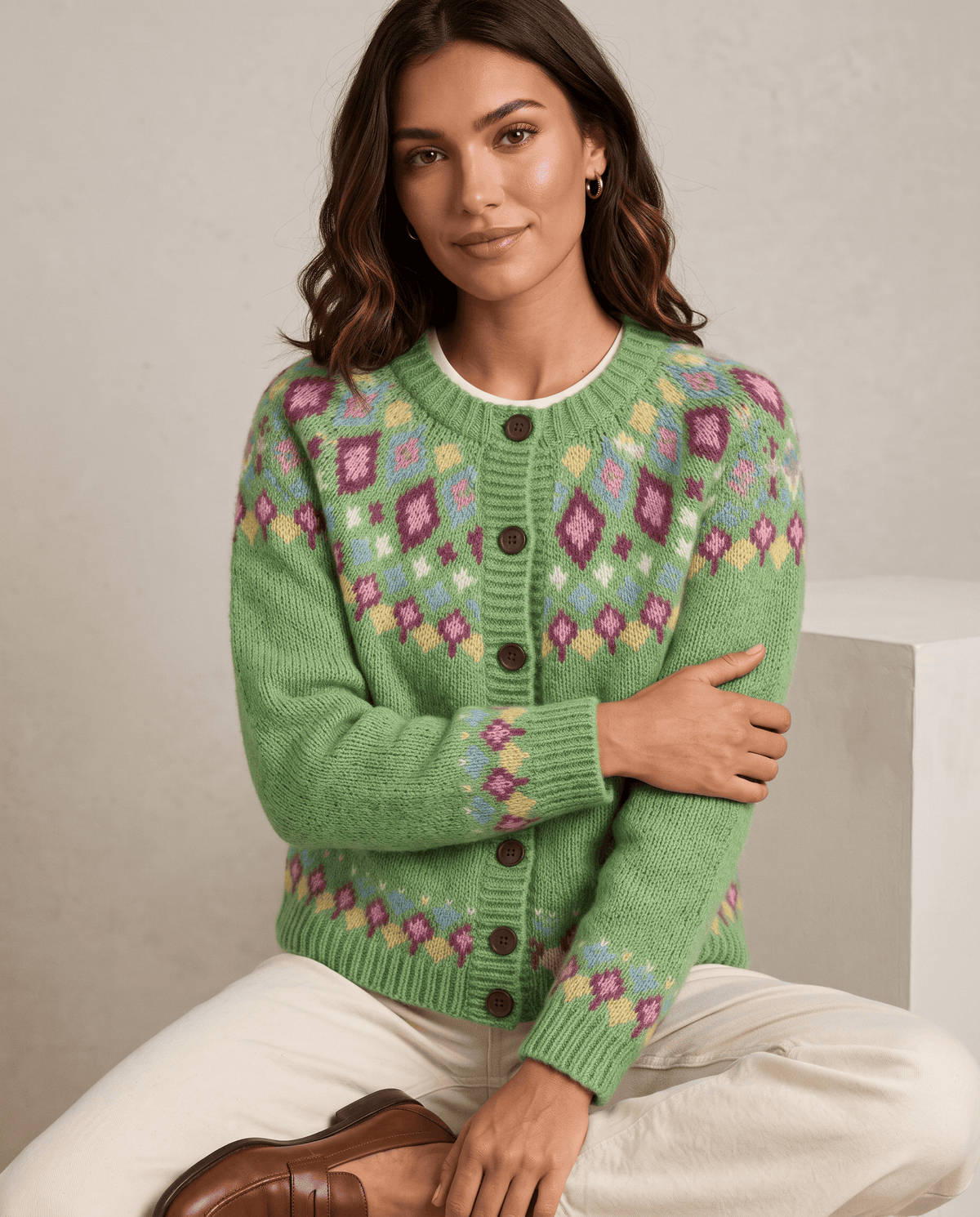 Woman seated in a green Fair Isle cardigan with a patterned yoke and hem