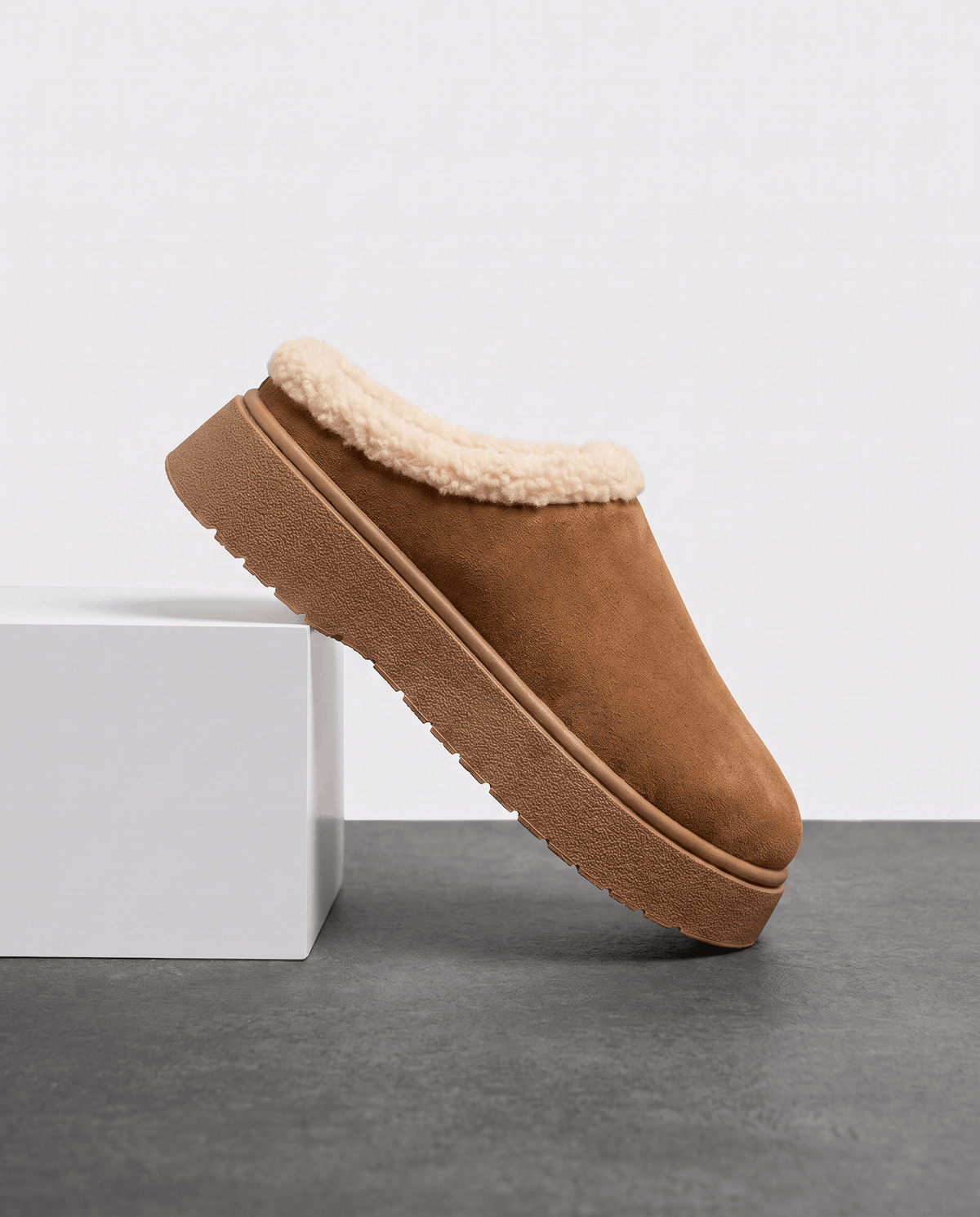 Brown fleece-lined slipper with a shearling-look cuff, displayed on a white pedestal.