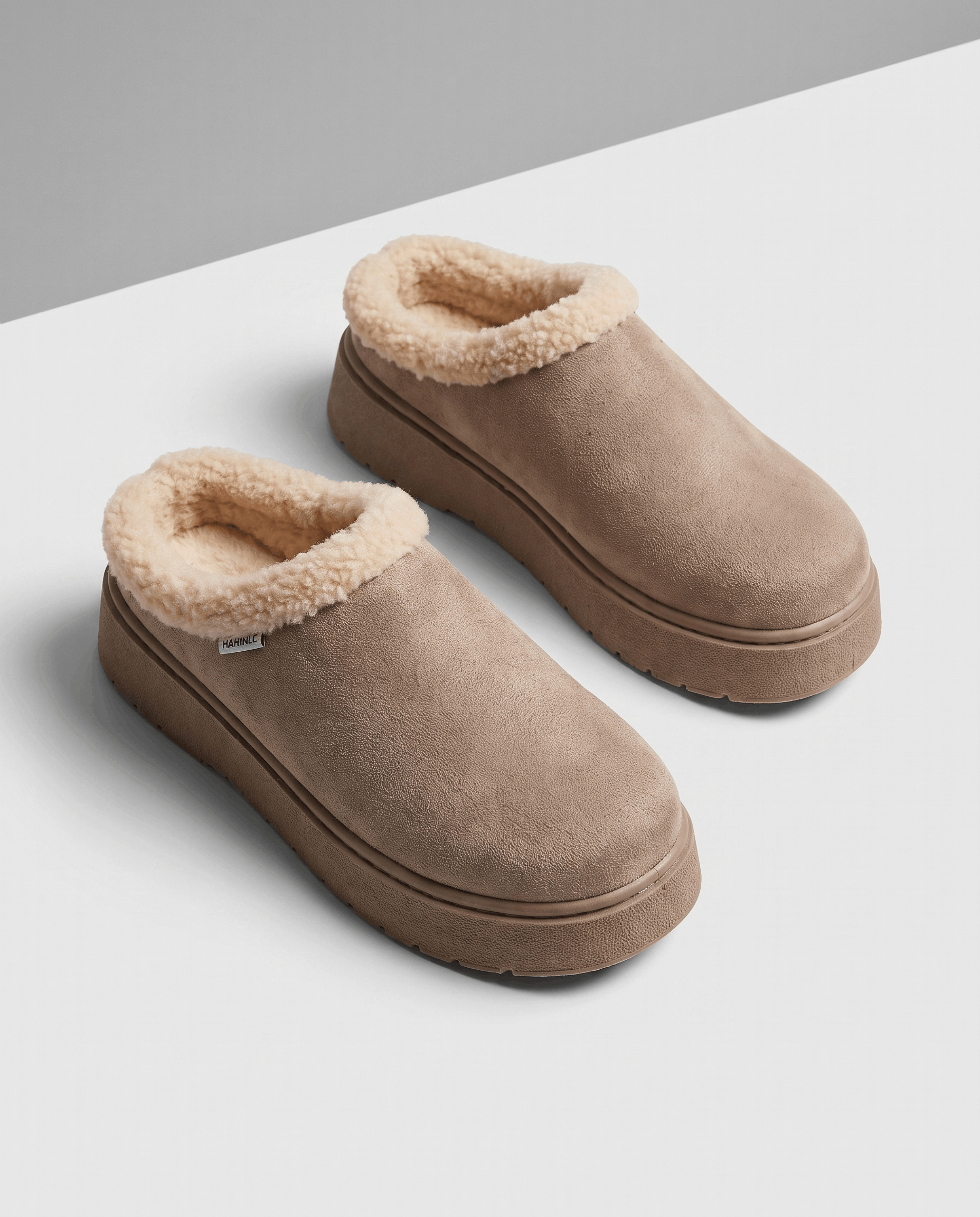 Pair of taupe slip-on slippers with a thick cream shearling-look lining and cushioned platform soles.