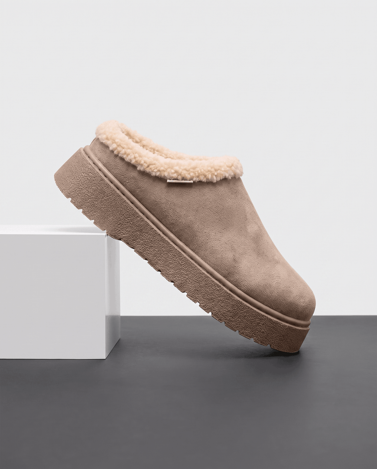 Taupe fleece-lined slipper with a shearling-look cuff, displayed on a white pedestal.