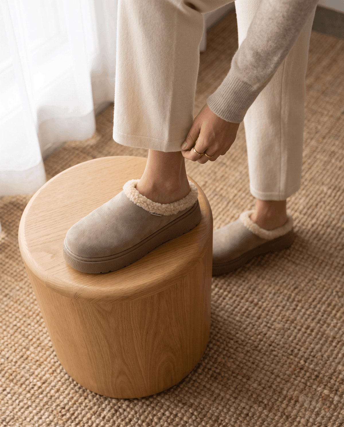 Close-up of a person wearing taupe slippers with a shearling-look cuff and platform sole.