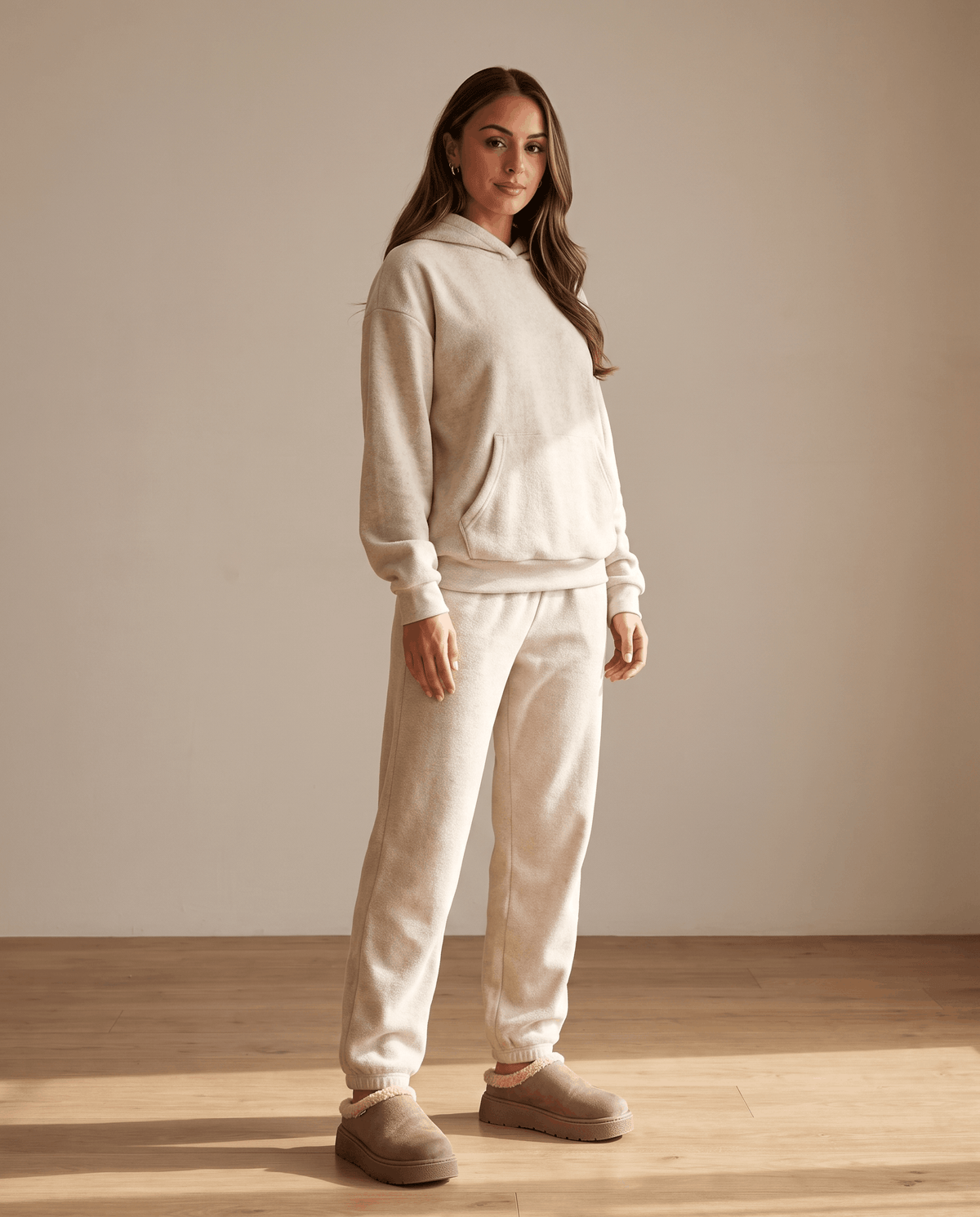 Woman wearing taupe shearling-look slippers with a cream lounge outfit.