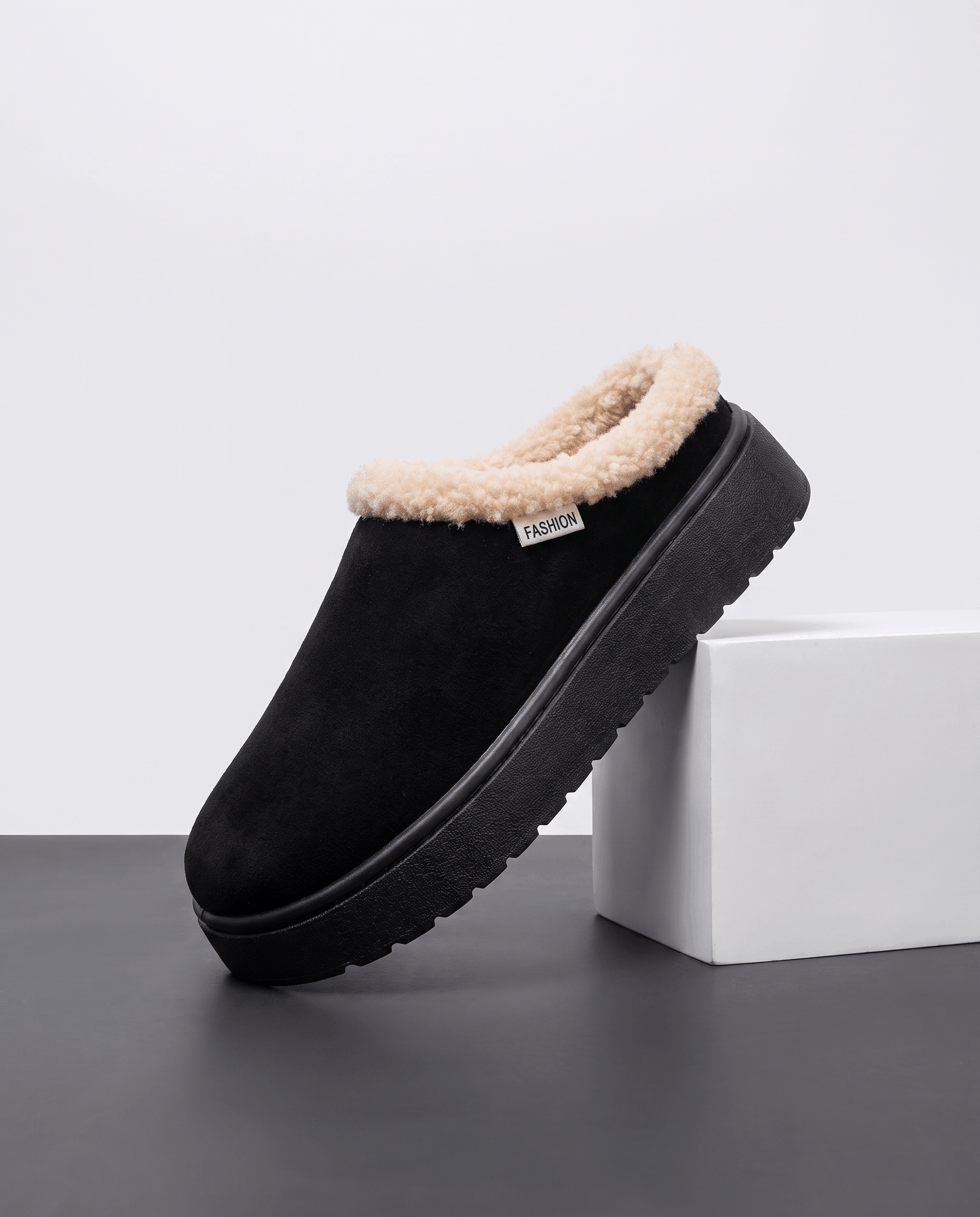 Black fleece-lined slipper with a shearling-look cuff, displayed on a white pedestal.