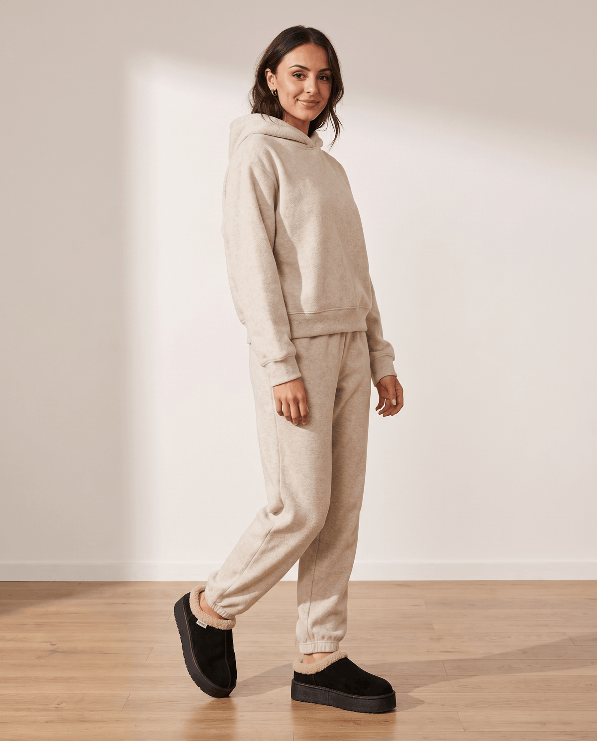 Woman wearing black shearling-look slippers with a cream lounge outfit.